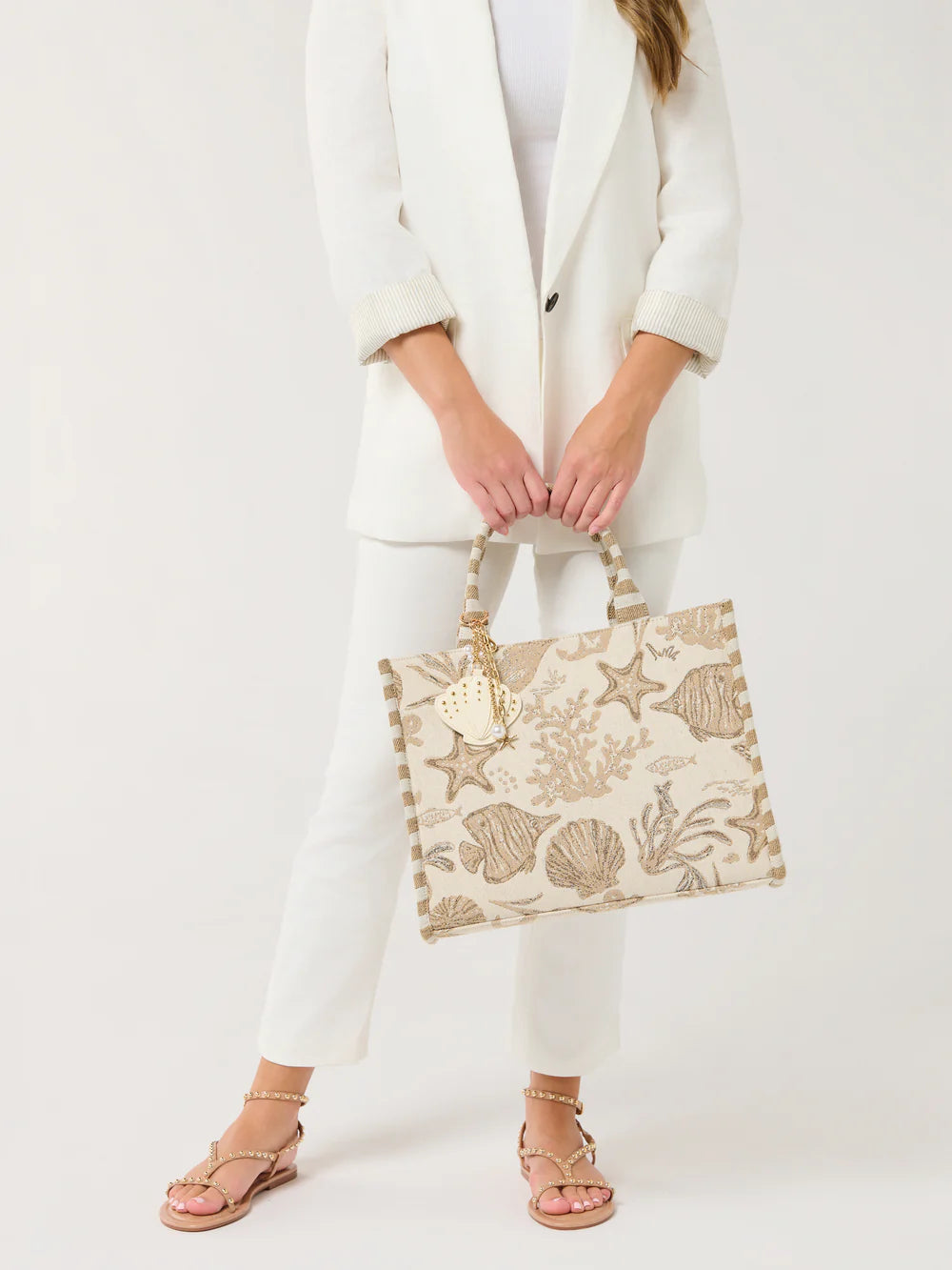 Person holding a decorative handbag with shell patterns on a white background