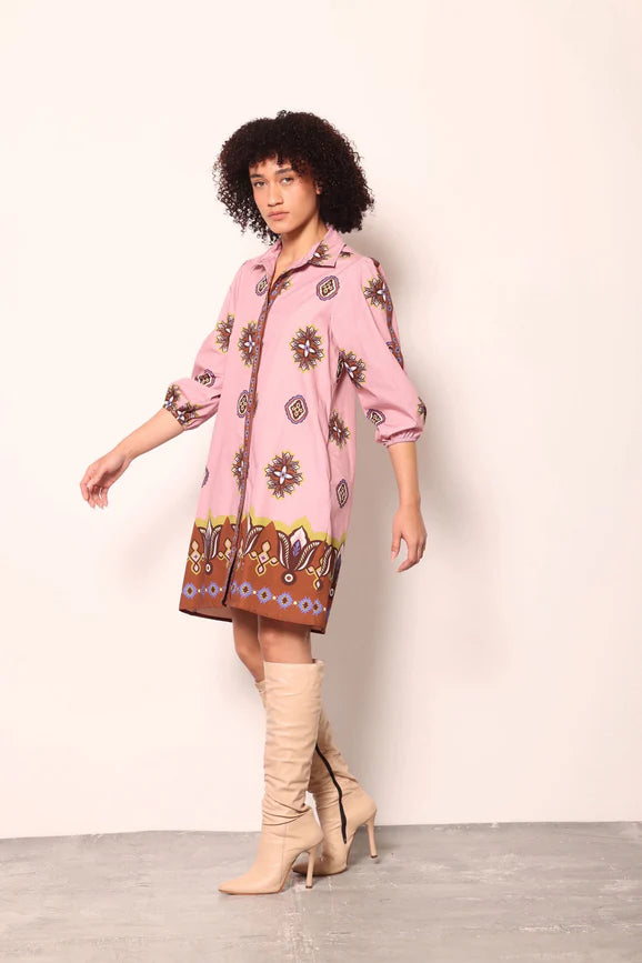 Woman wearing a pink patterned dress with beige knee-high boots on a plain background