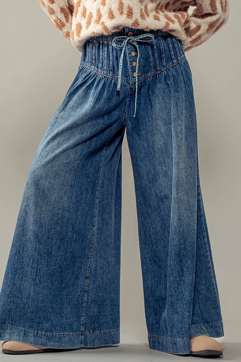Wide-leg blue jeans worn with a patterned top on a neutral background