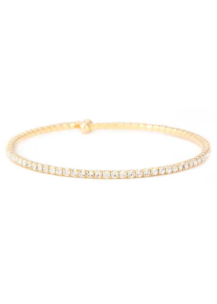 A delicate gold bangle bracelet featuring a single row of small clear stones along the front, displayed against a solid white background.