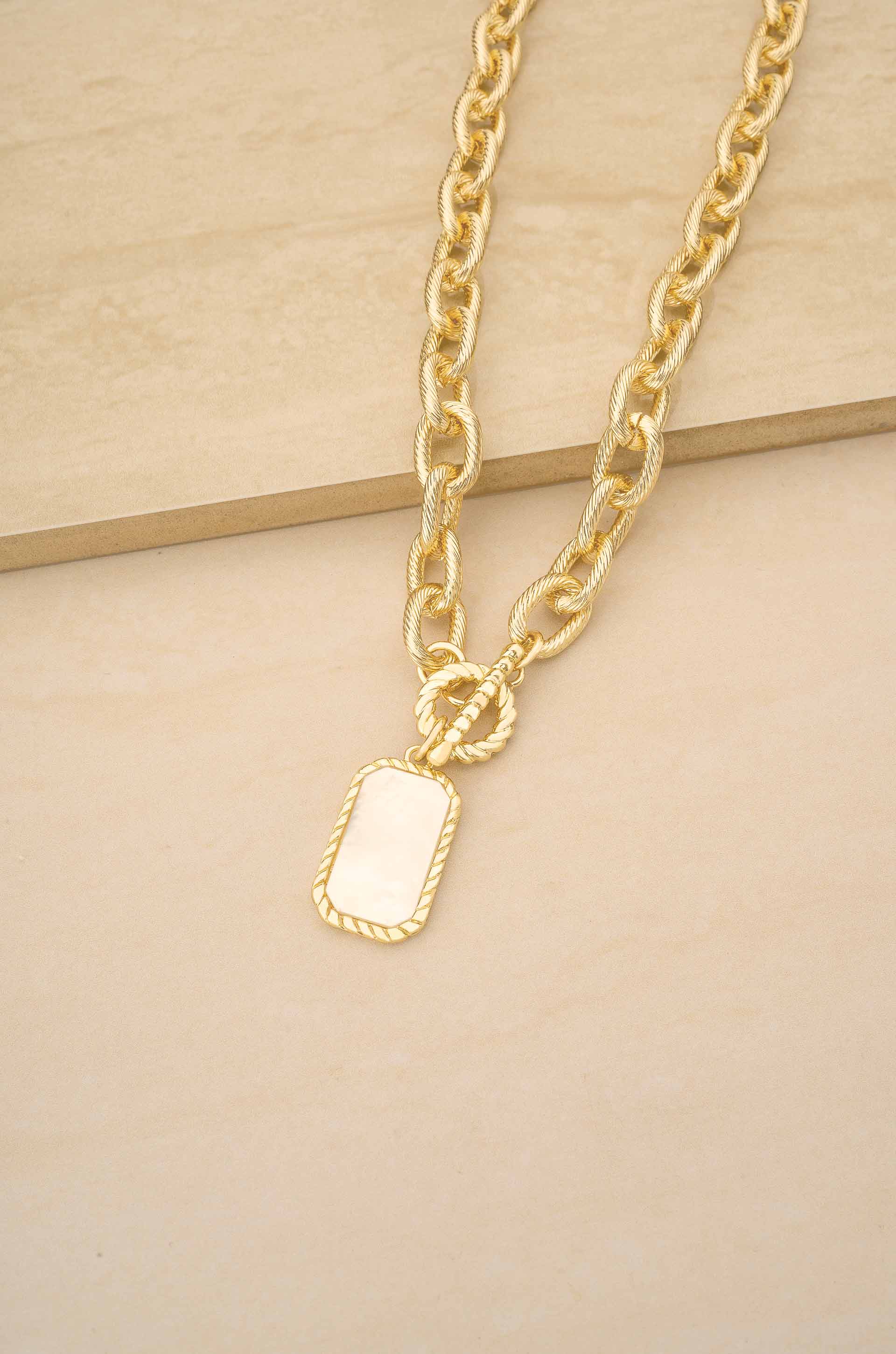 Gold chain necklace with a rectangular pendant on a beige background