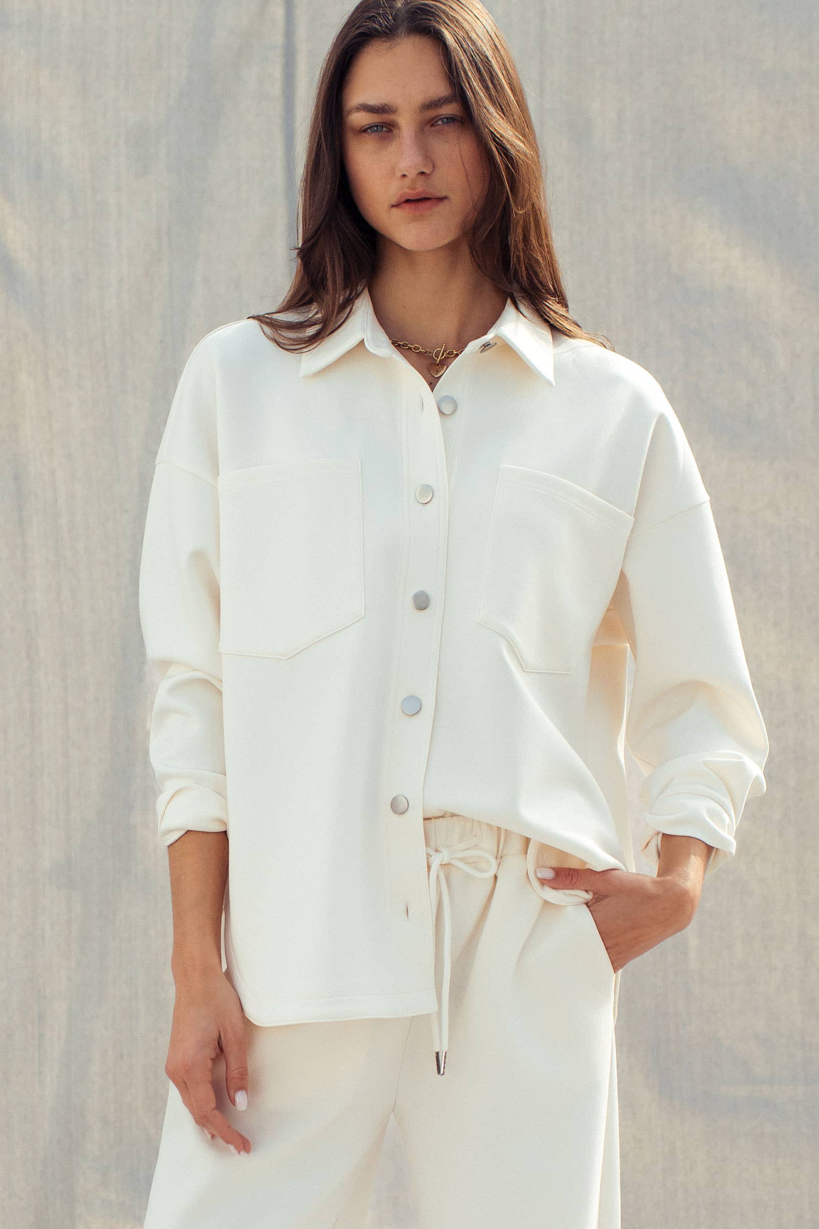 Woman wearing a white button-up shirt and pants against a neutral background