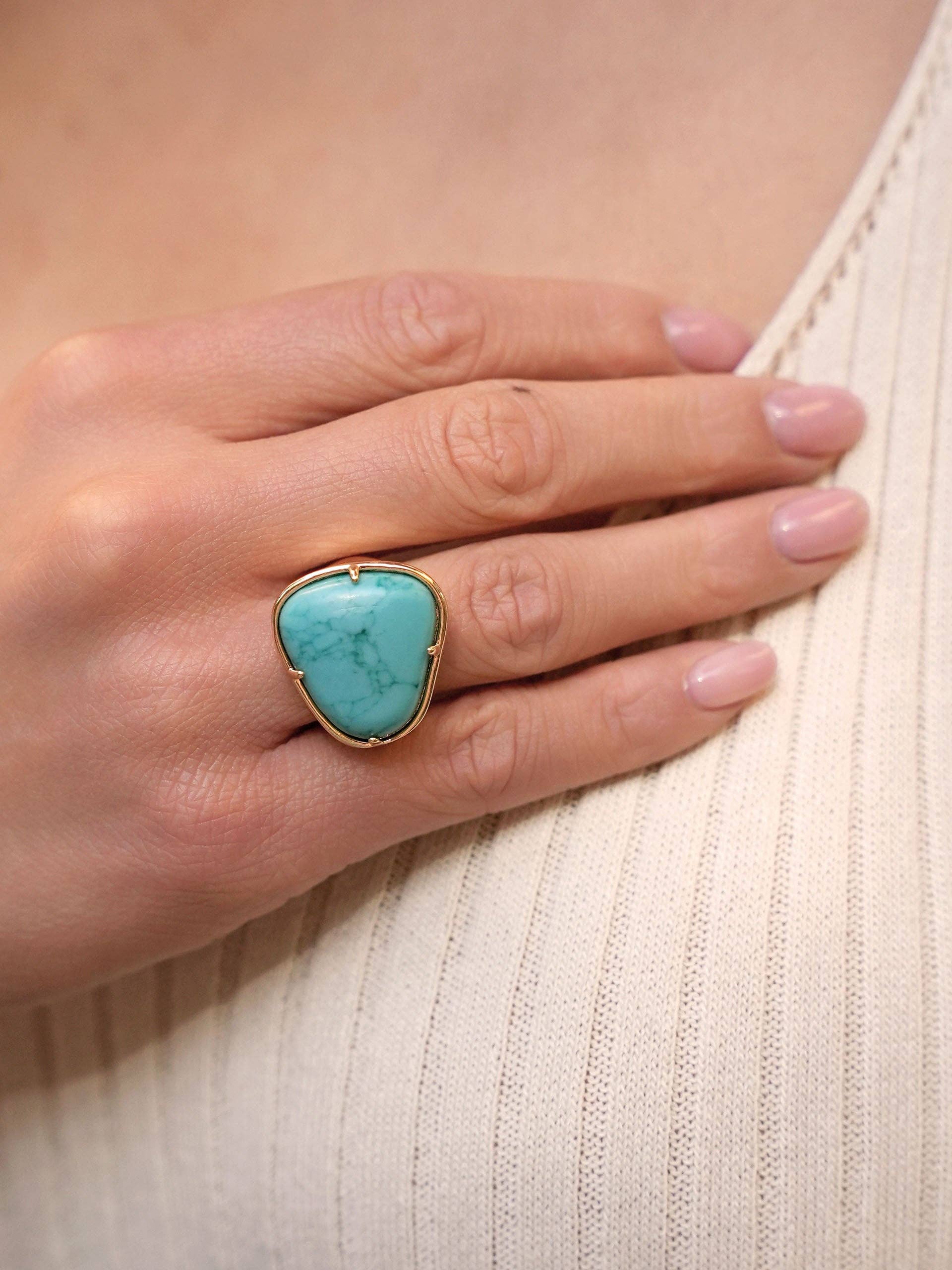 Hand wearing a turquoise ring on a light background