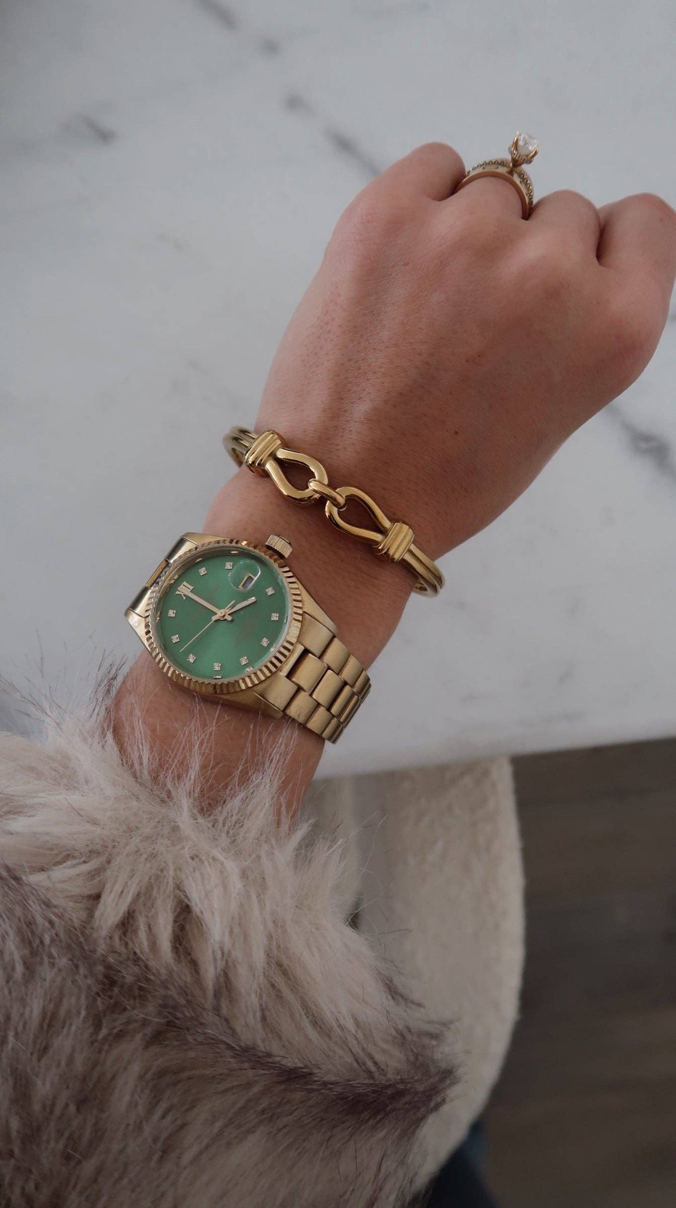 Gold watch and bracelet on a wrist with a neutral background