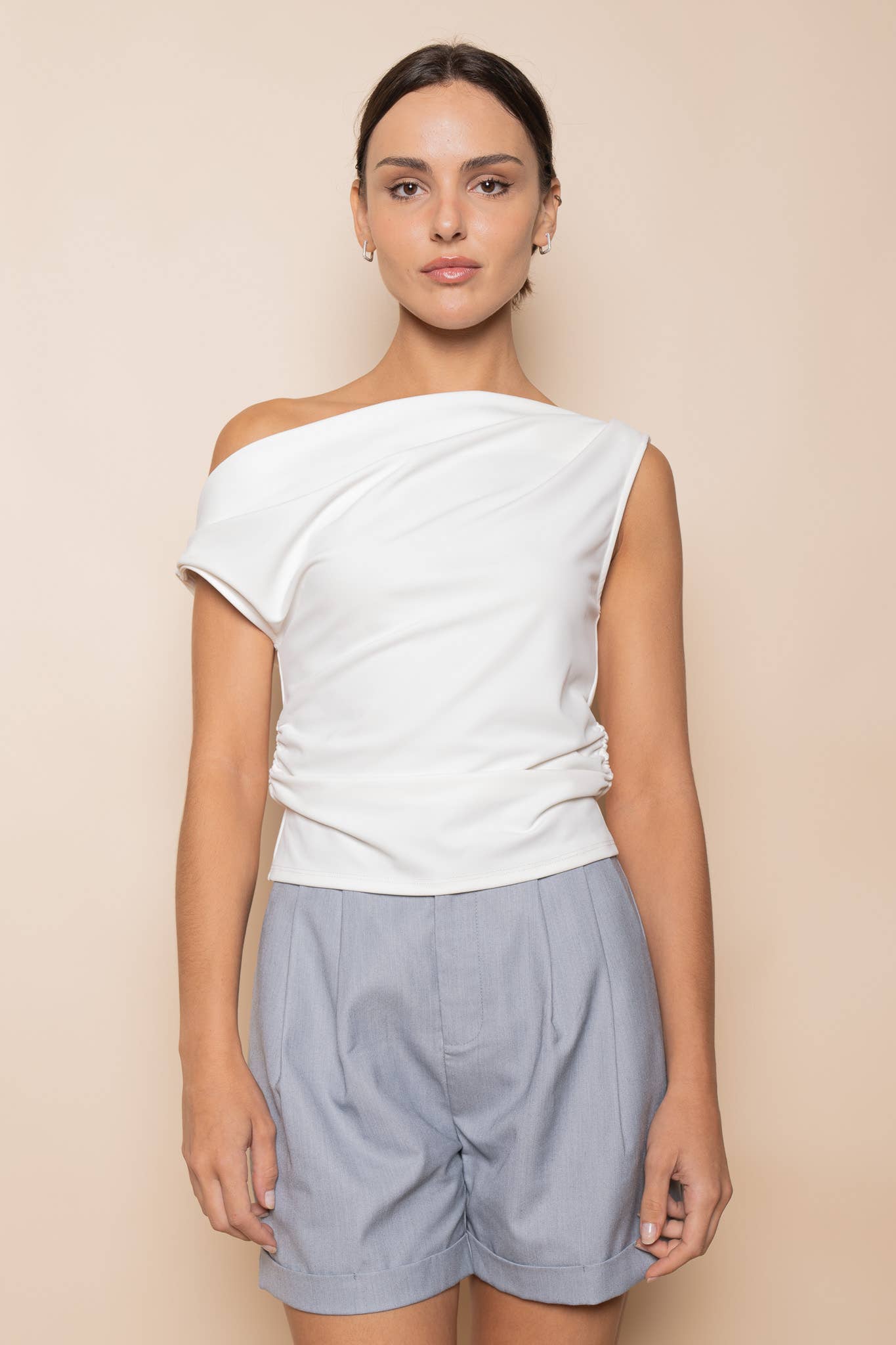 Woman wearing a white off-shoulder top and light gray shorts on a beige background