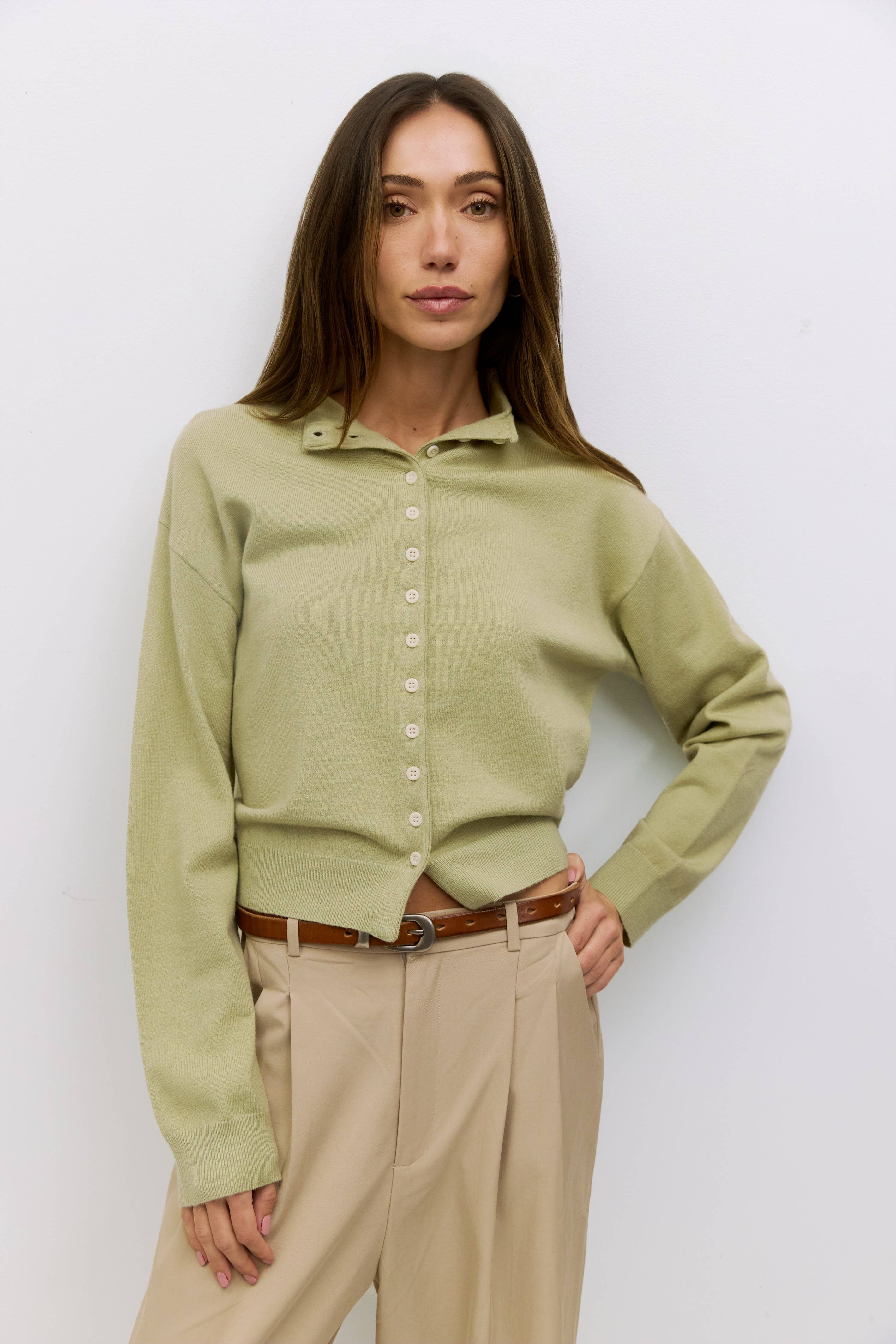 Woman wearing a light green blouse and beige pants against a white background