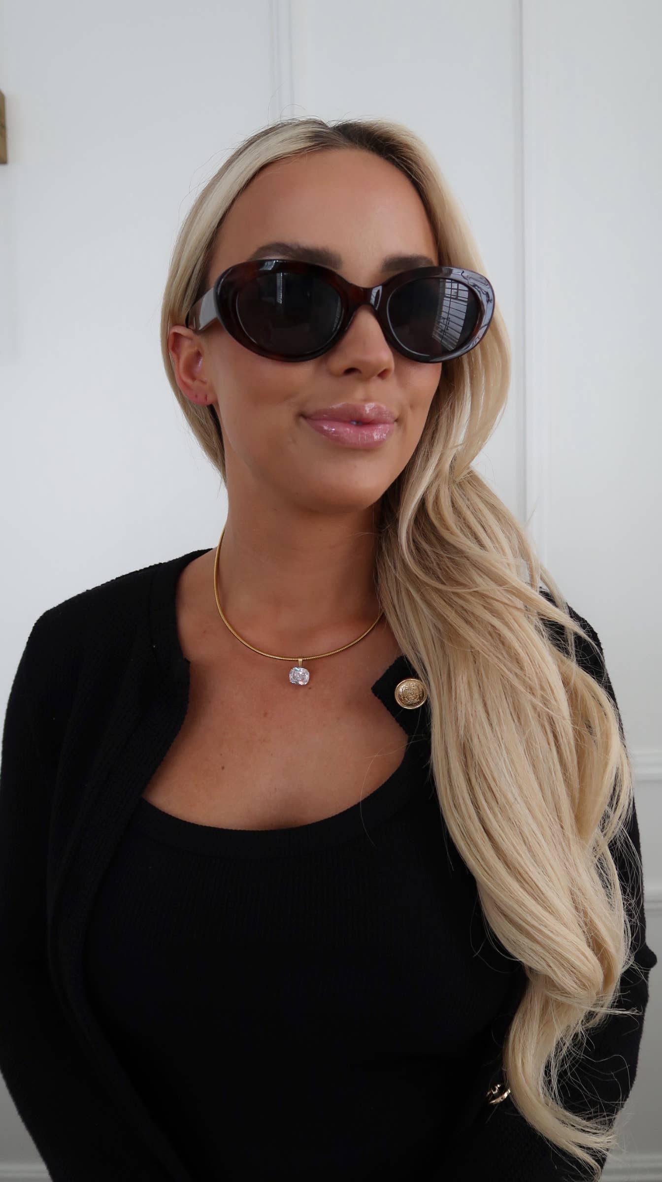 Woman wearing sunglasses and a black outfit against a white background