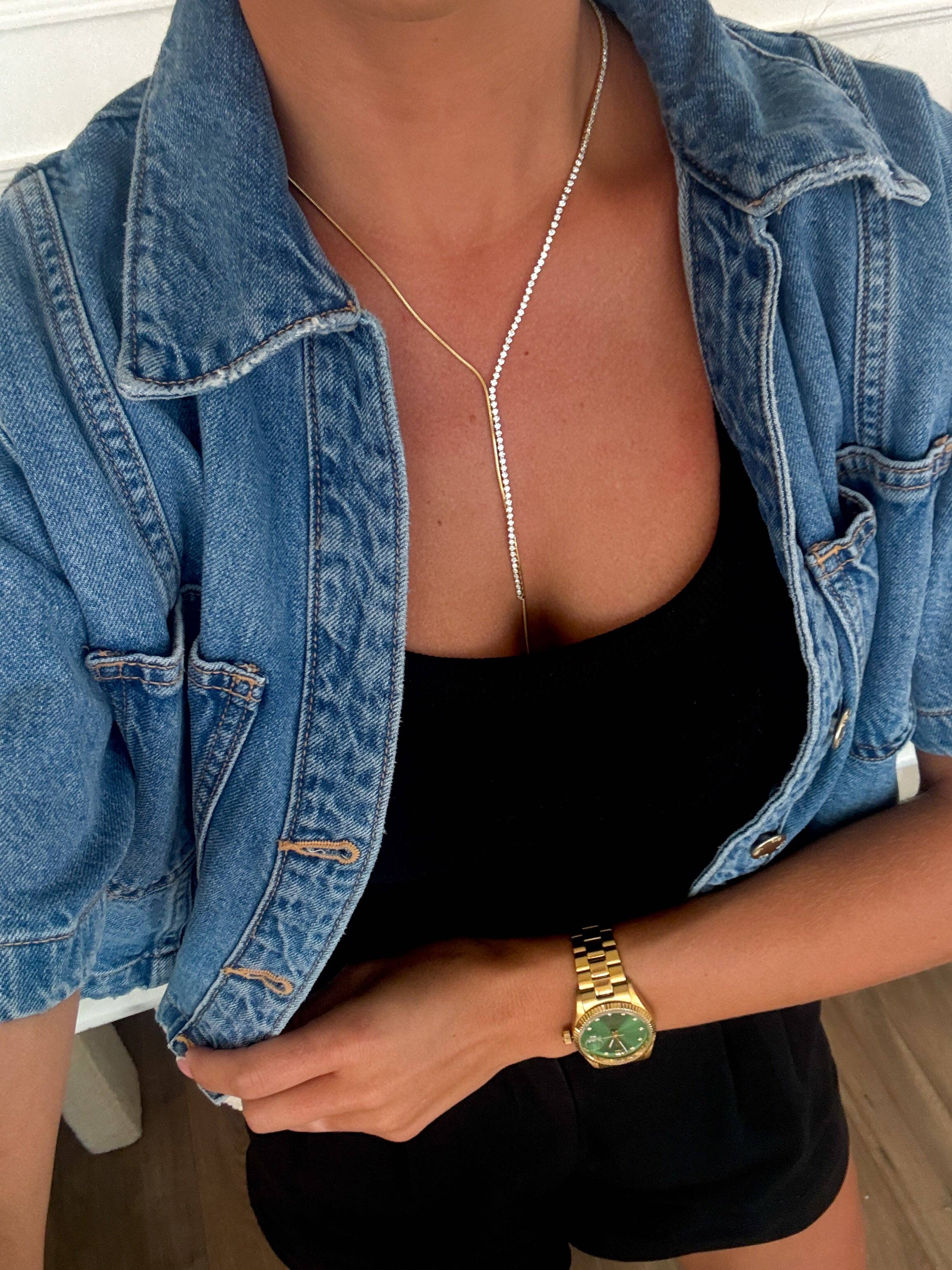Person wearing a denim jacket over a black top, gold necklace, and gold watch.