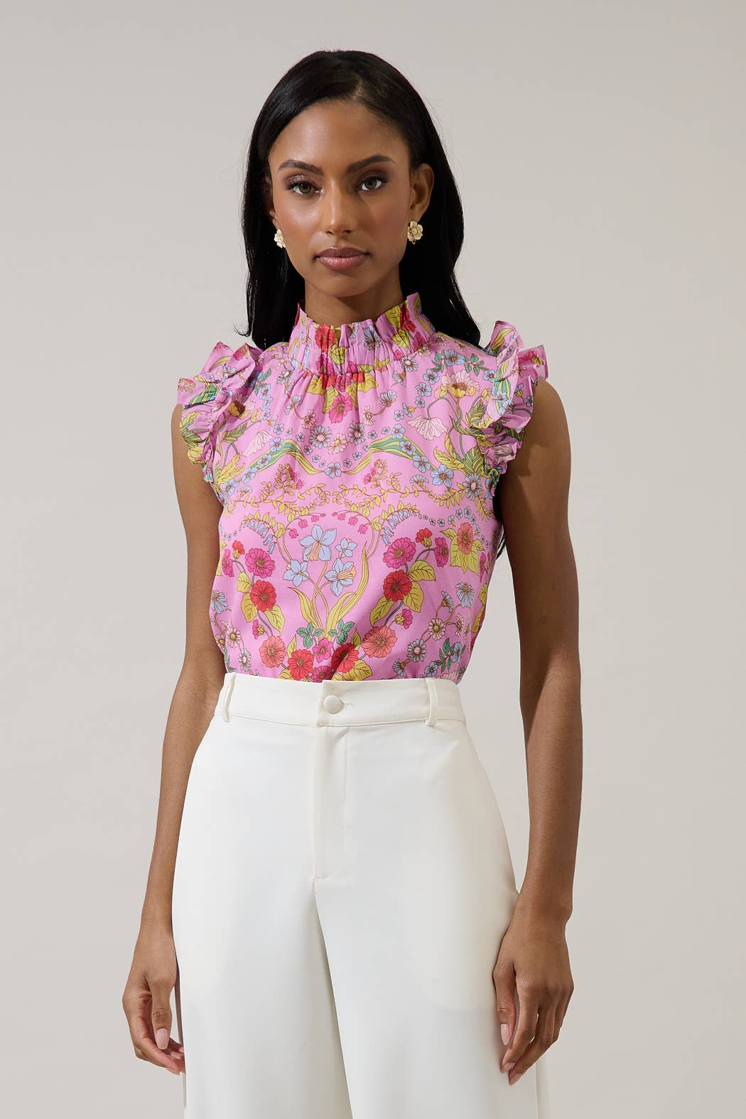 Woman wearing a pink floral top and white pants against a plain background