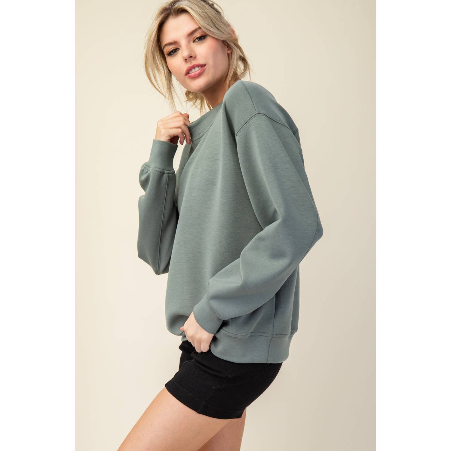 Woman wearing a light blue sweatshirt and black shorts on a beige background