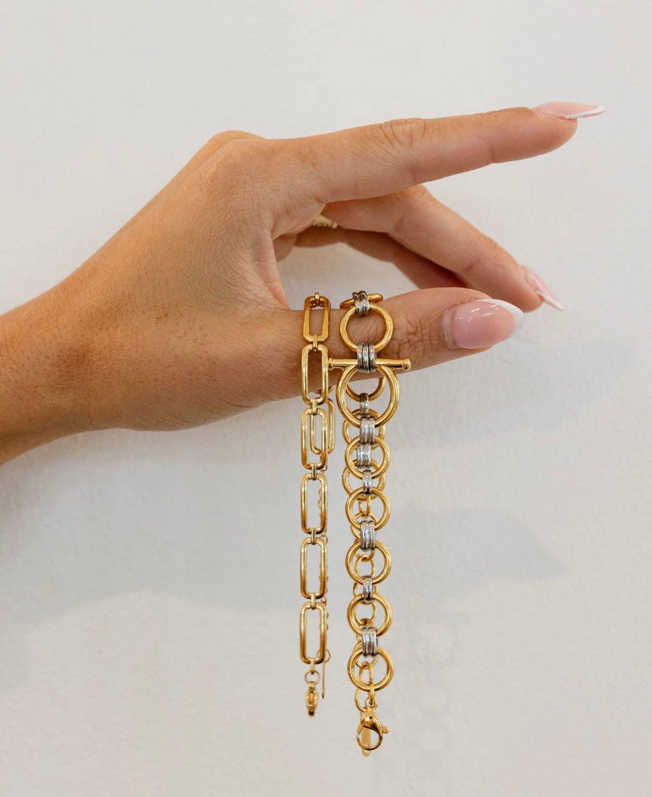 Gold chain bracelet held by a hand against a plain background