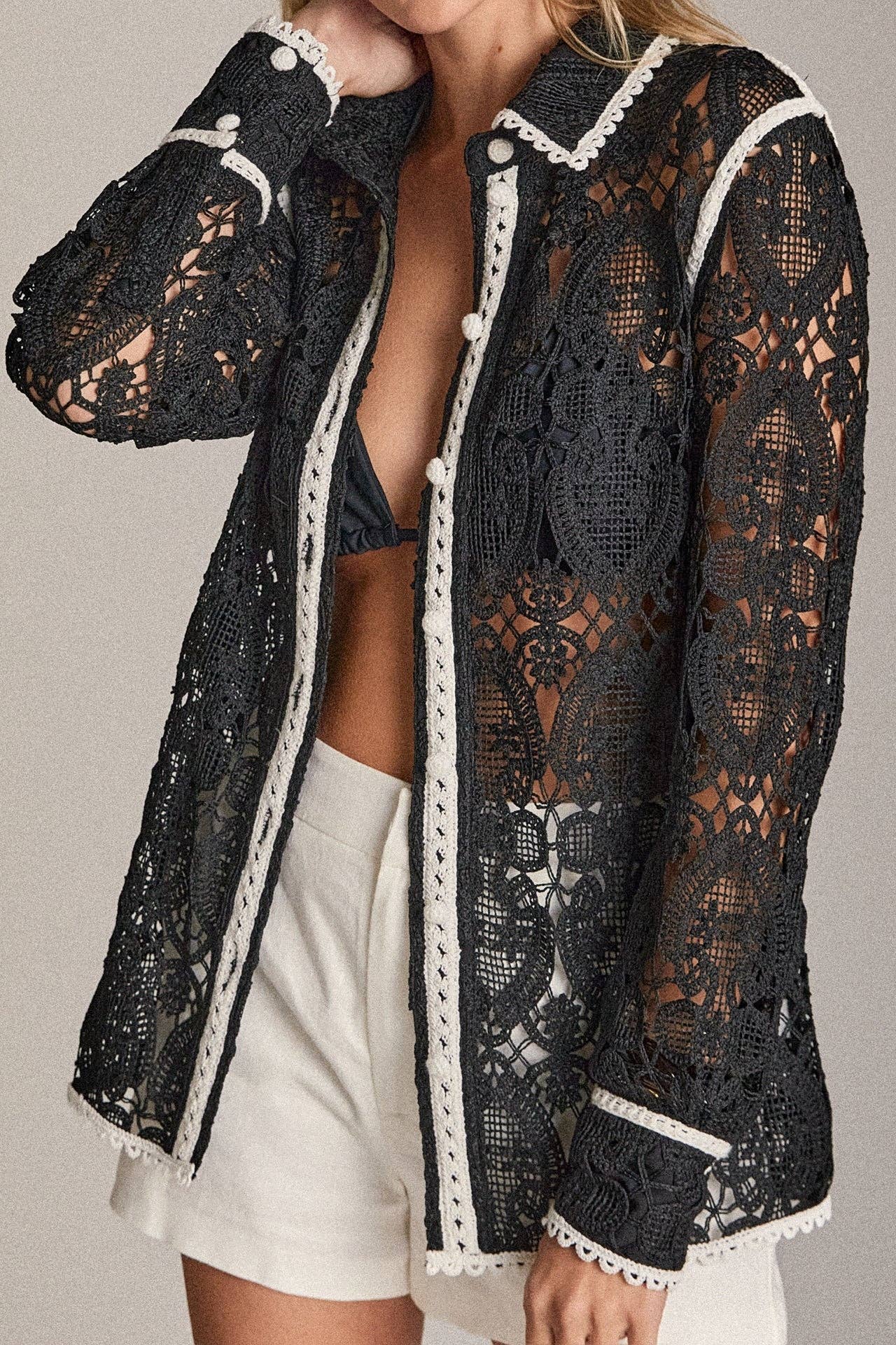 Black lace jacket with white trim worn by a person on a neutral background