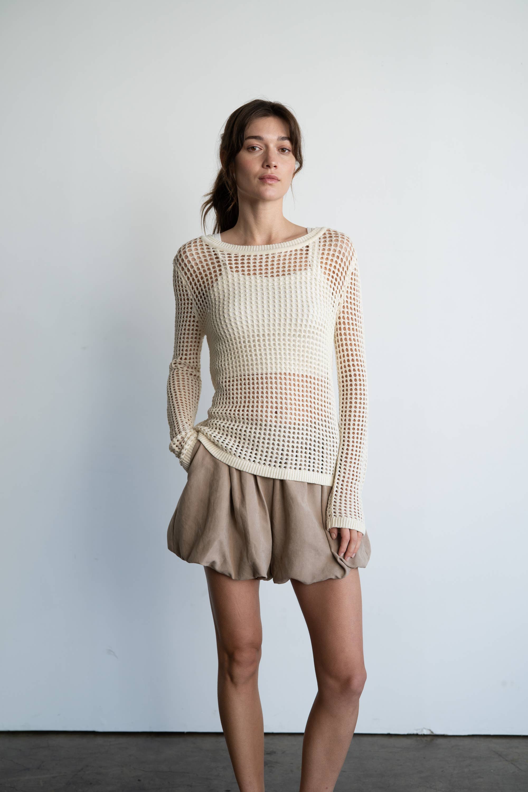Woman wearing a textured white top and beige skirt against a plain background