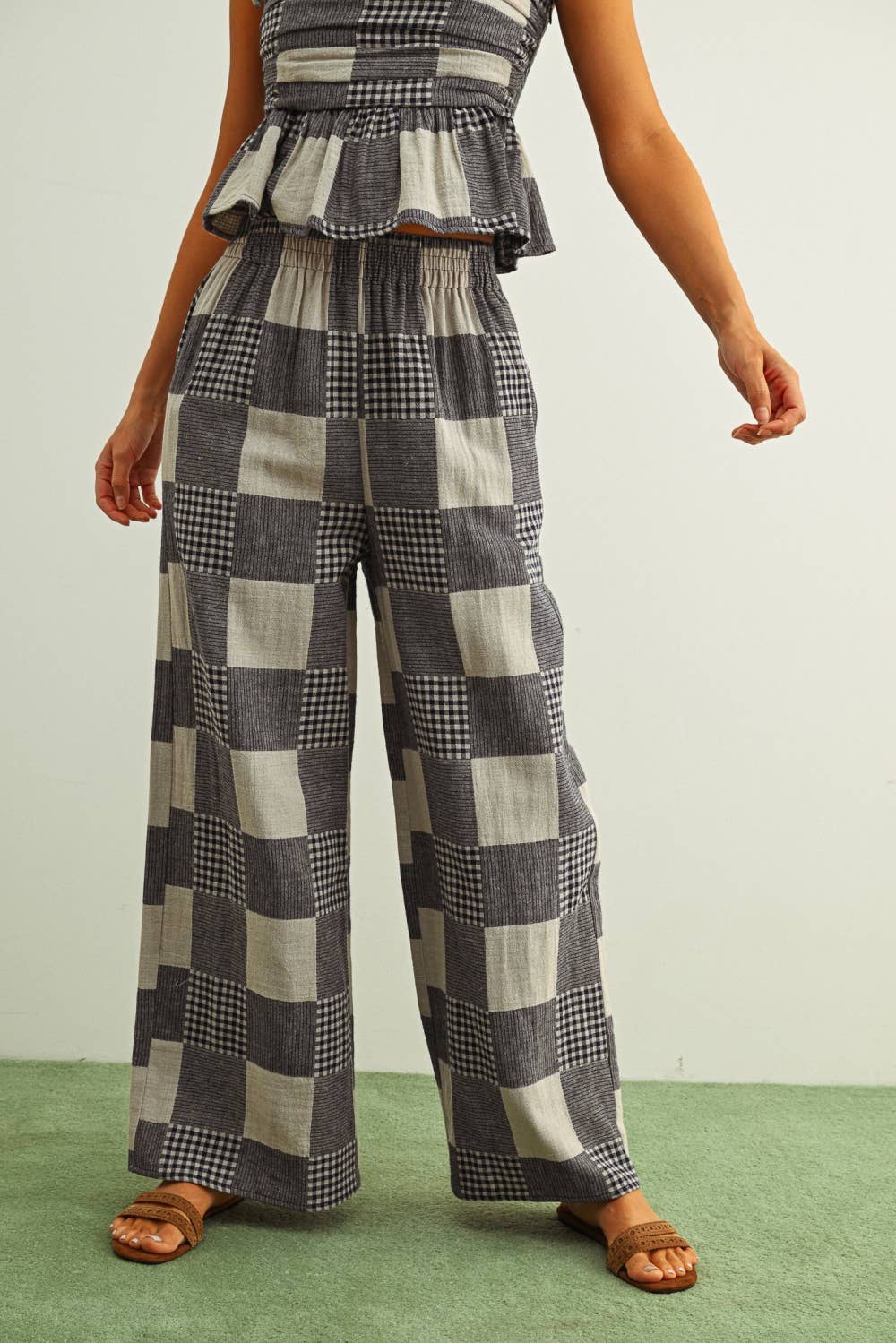Person wearing a checkered outfit with wide-leg pants and a peplum top on a plain background