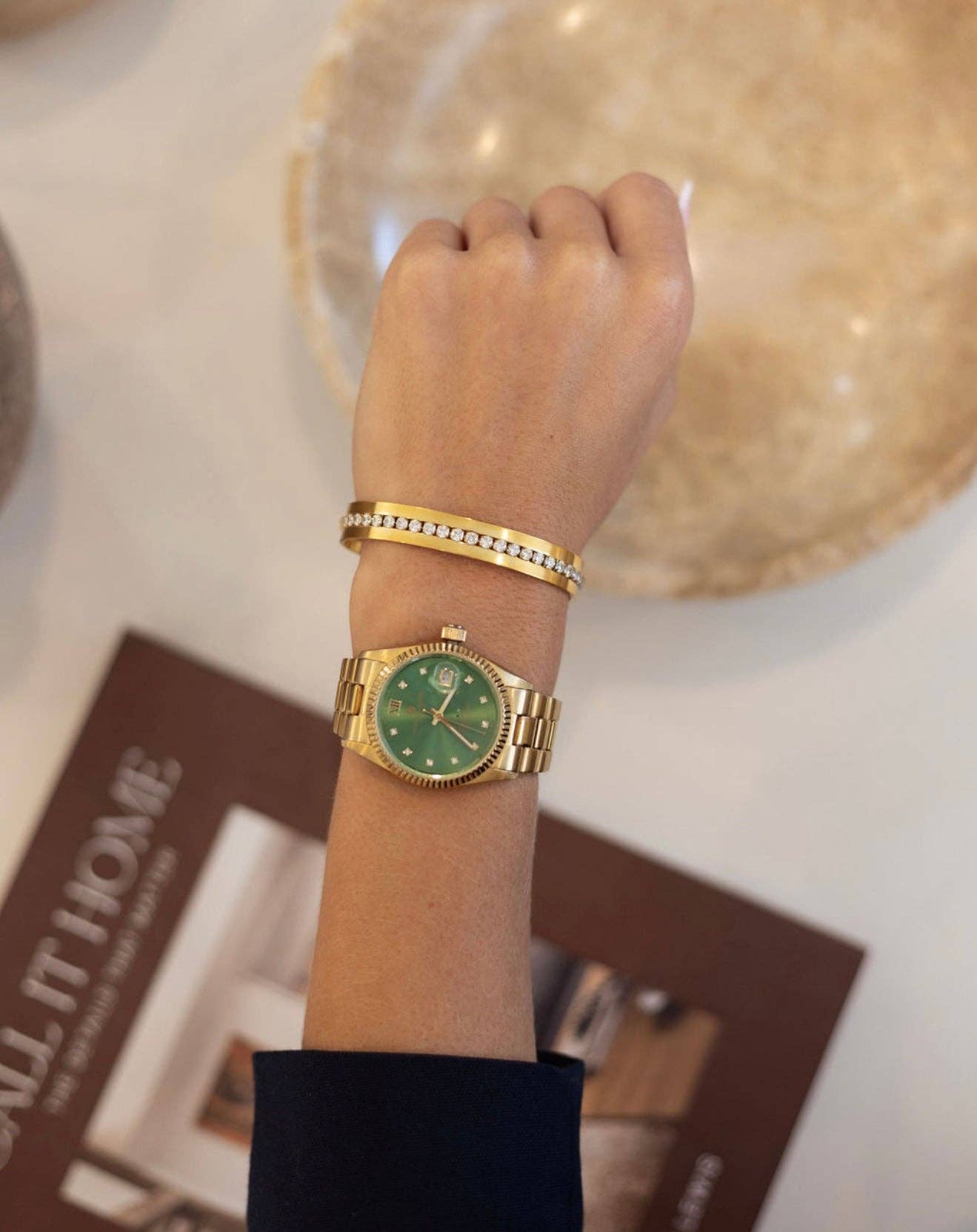 Gold watch with a green face on a wrist, with a blurred background