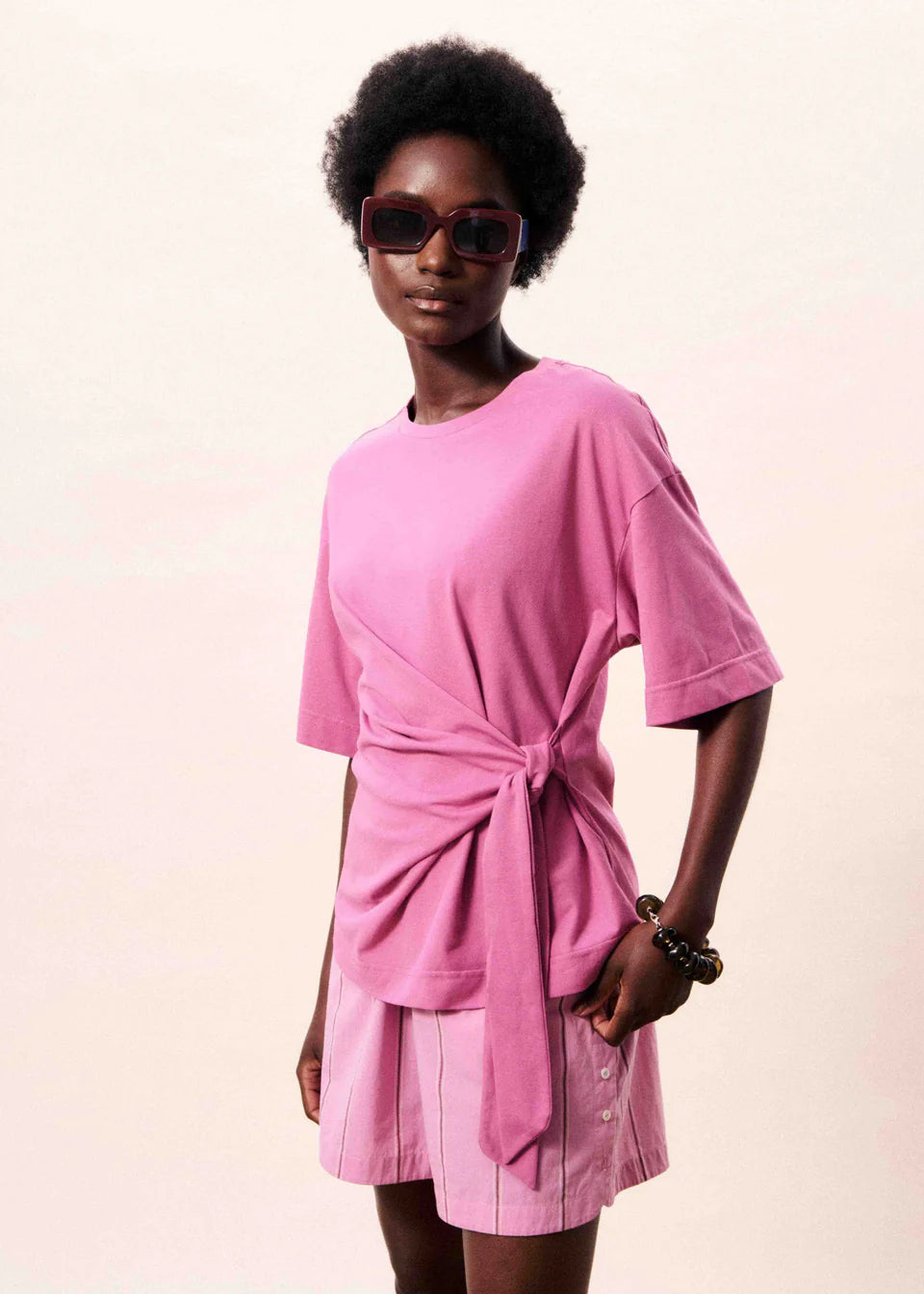 Woman wearing a pink dress with a tie waist on a plain background