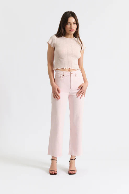 Woman wearing a beige top and light pink jeans on a white background