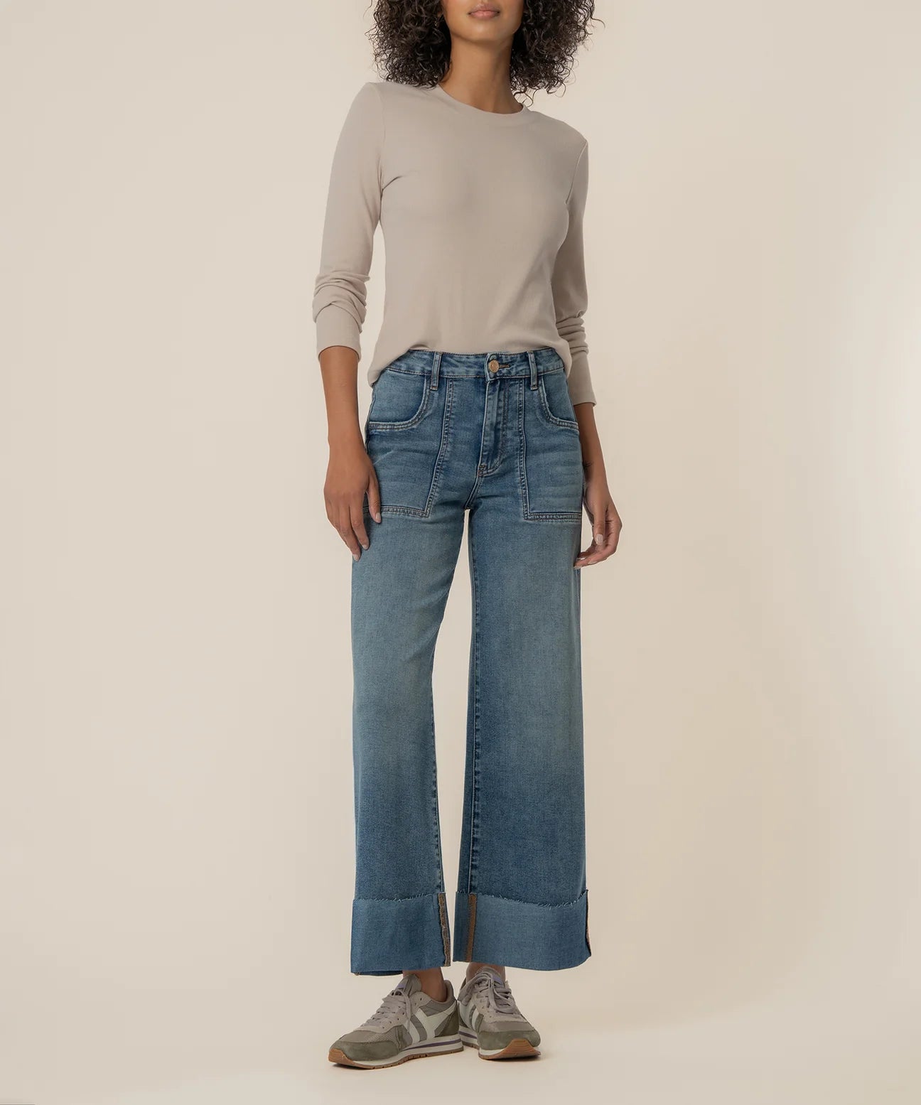 Person wearing a beige sweater and blue jeans on a plain background