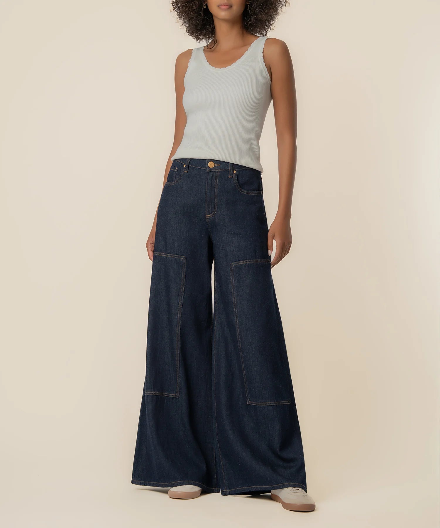 Woman wearing wide-leg jeans and a light gray tank top on a beige background