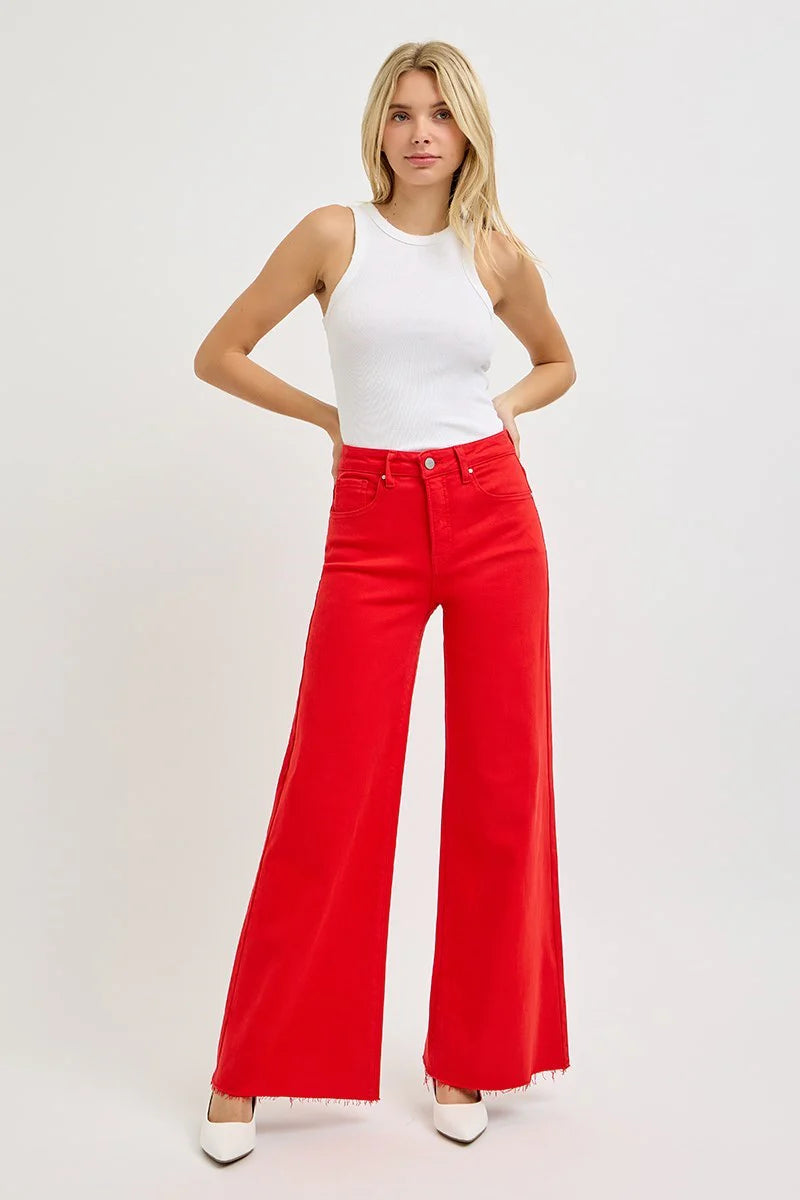Woman wearing a white top and red high-waisted jeans on a plain background