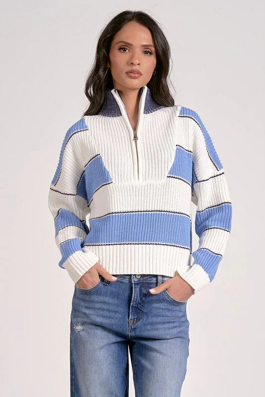 Woman wearing a blue and white striped sweater with a zipper on a plain background