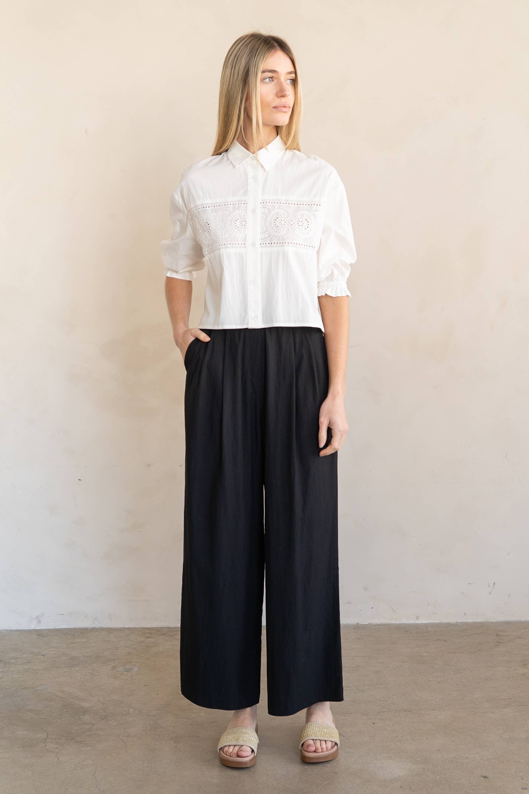 Woman wearing a white blouse and black pants against a plain background