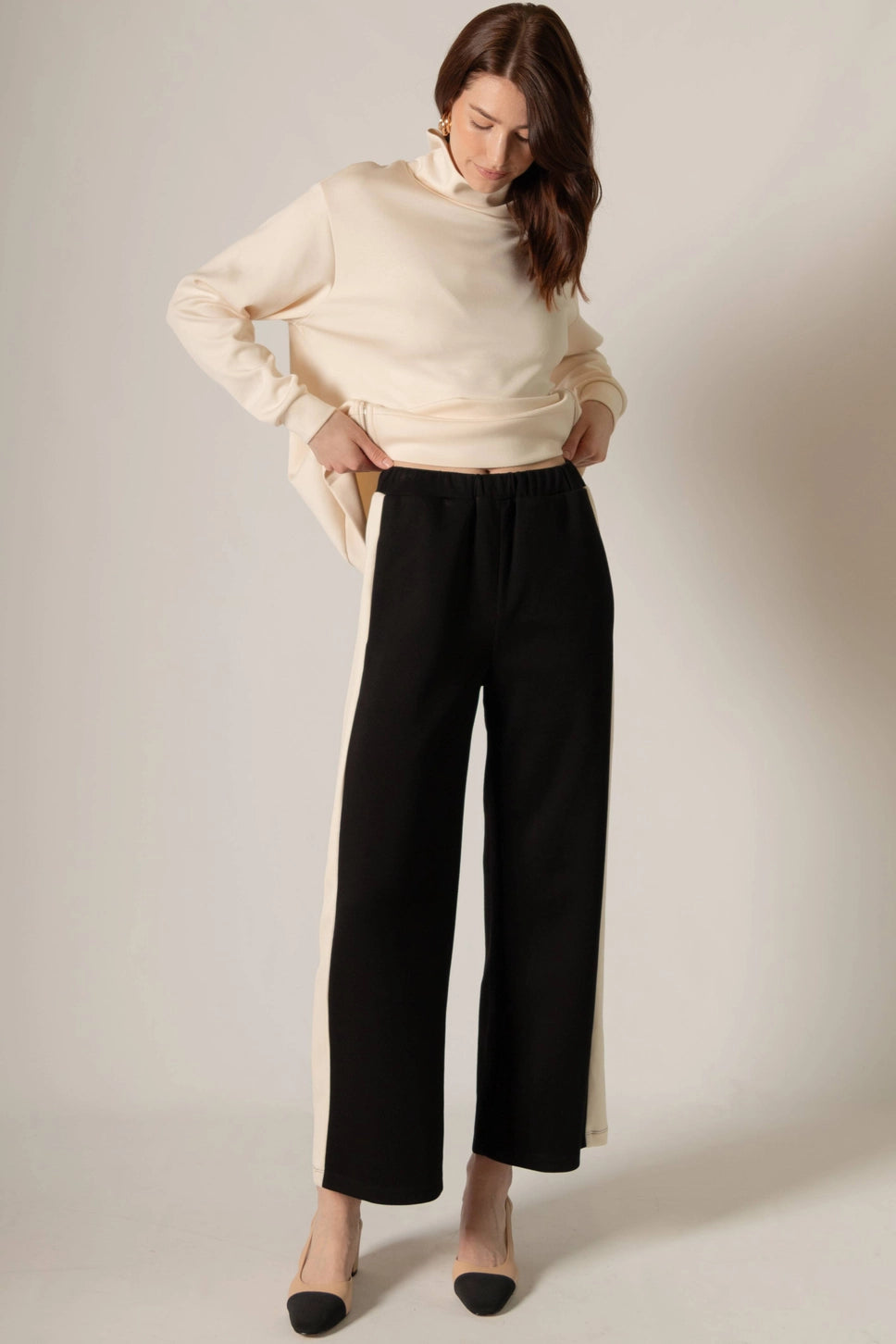 Woman wearing a cream sweater and black pants against a plain background