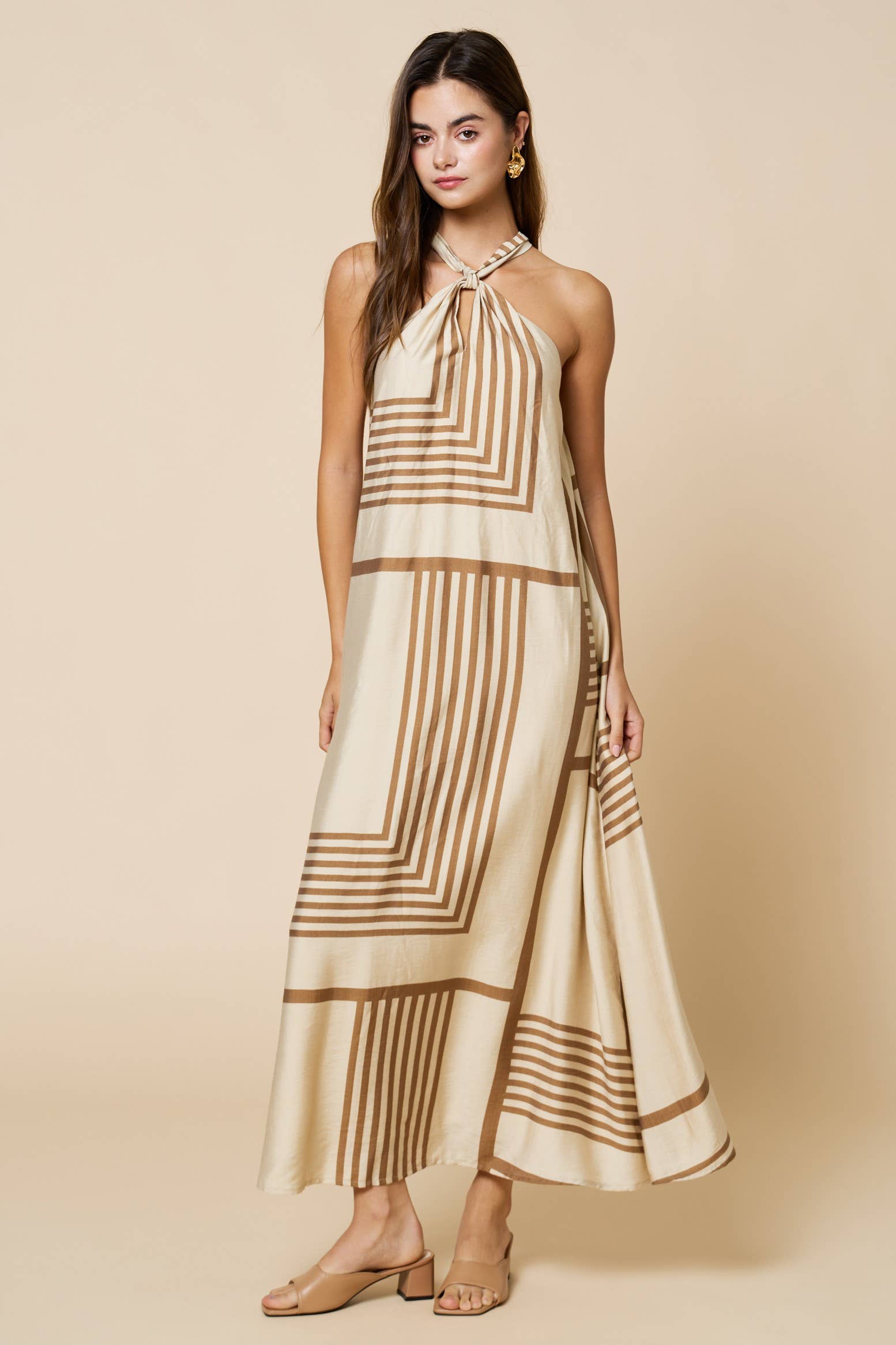 Woman wearing a beige and brown patterned halter neck dress on a beige background