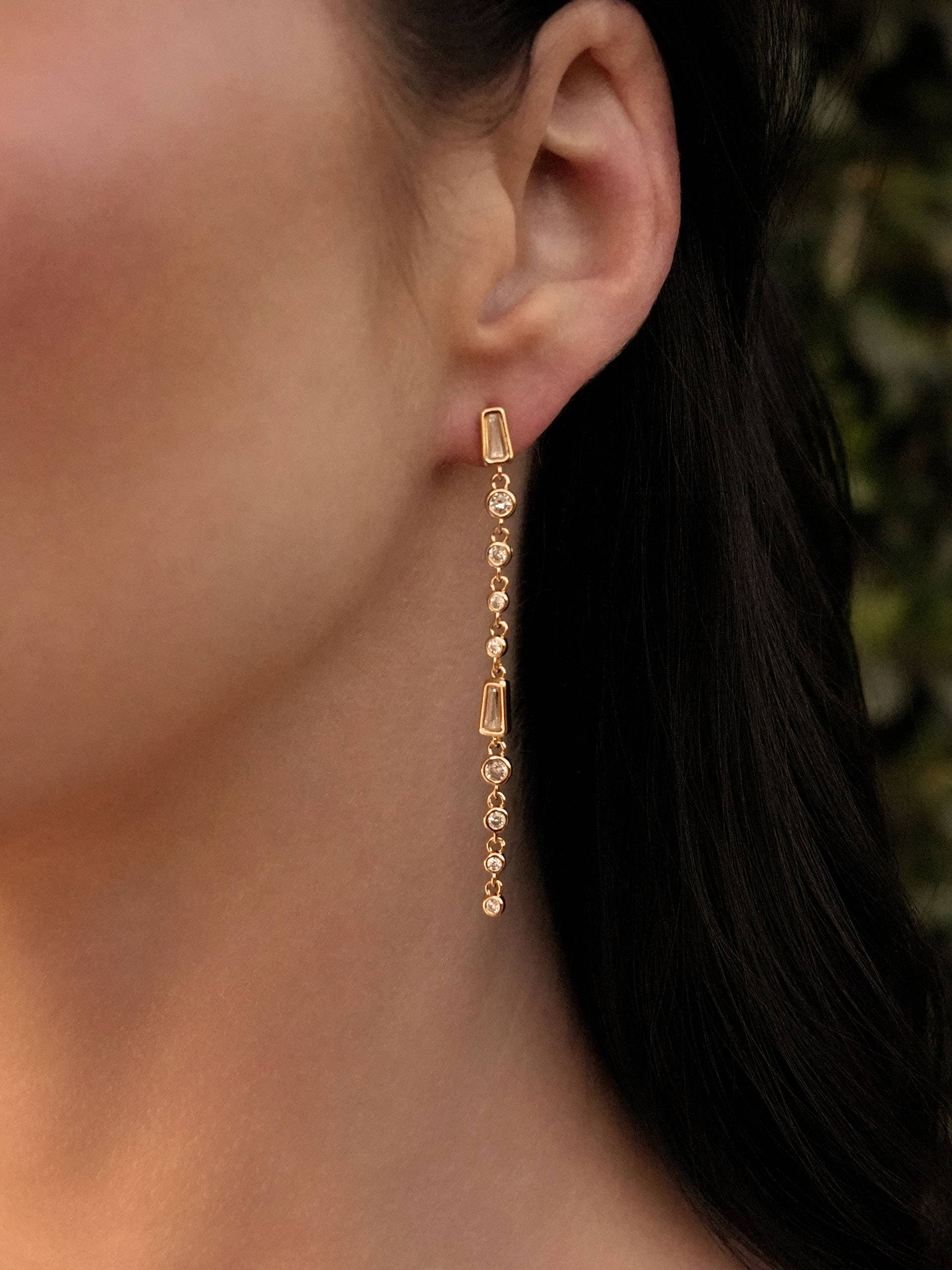 Gold chain earring worn by a person with a blurred background