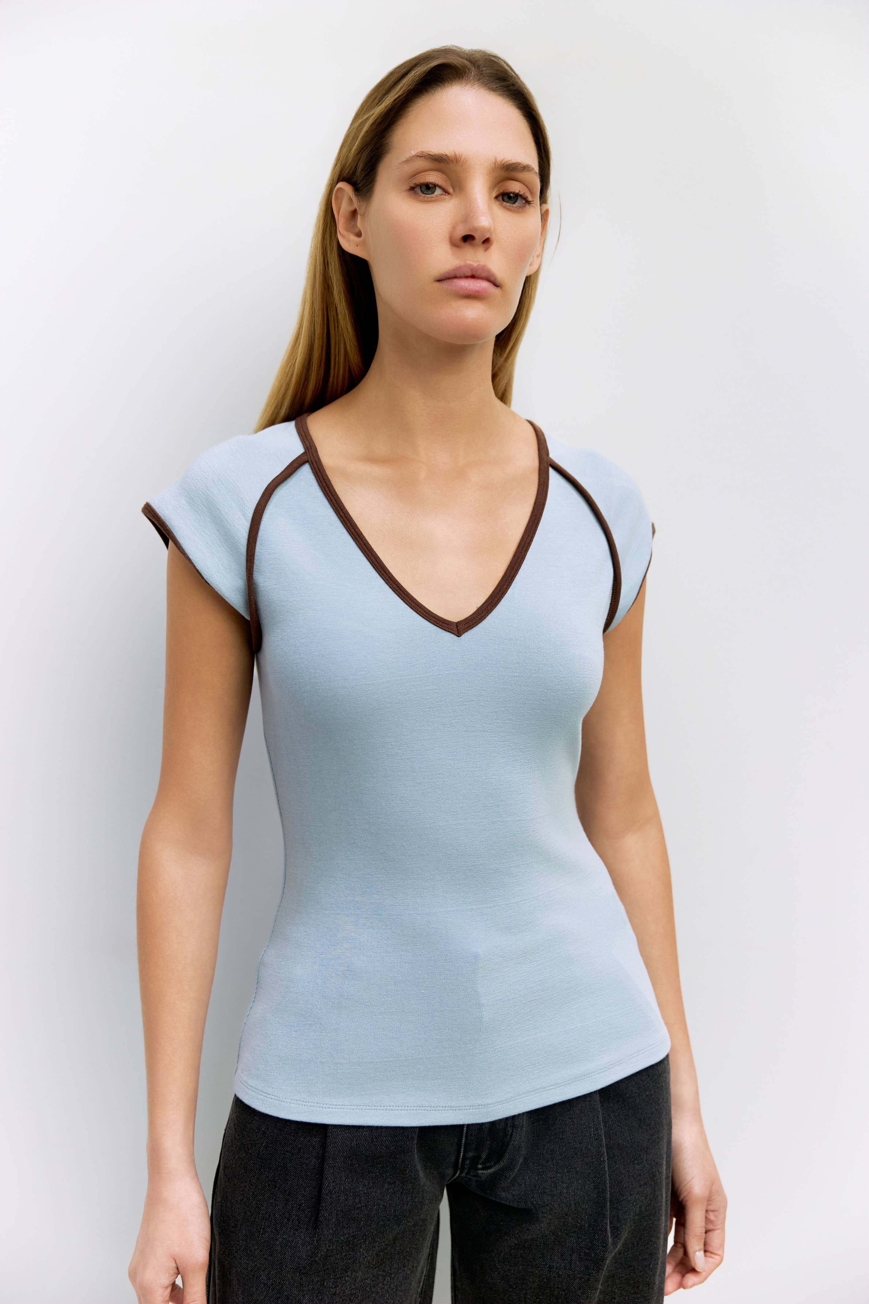 Woman wearing a light blue top with brown trim on a white background