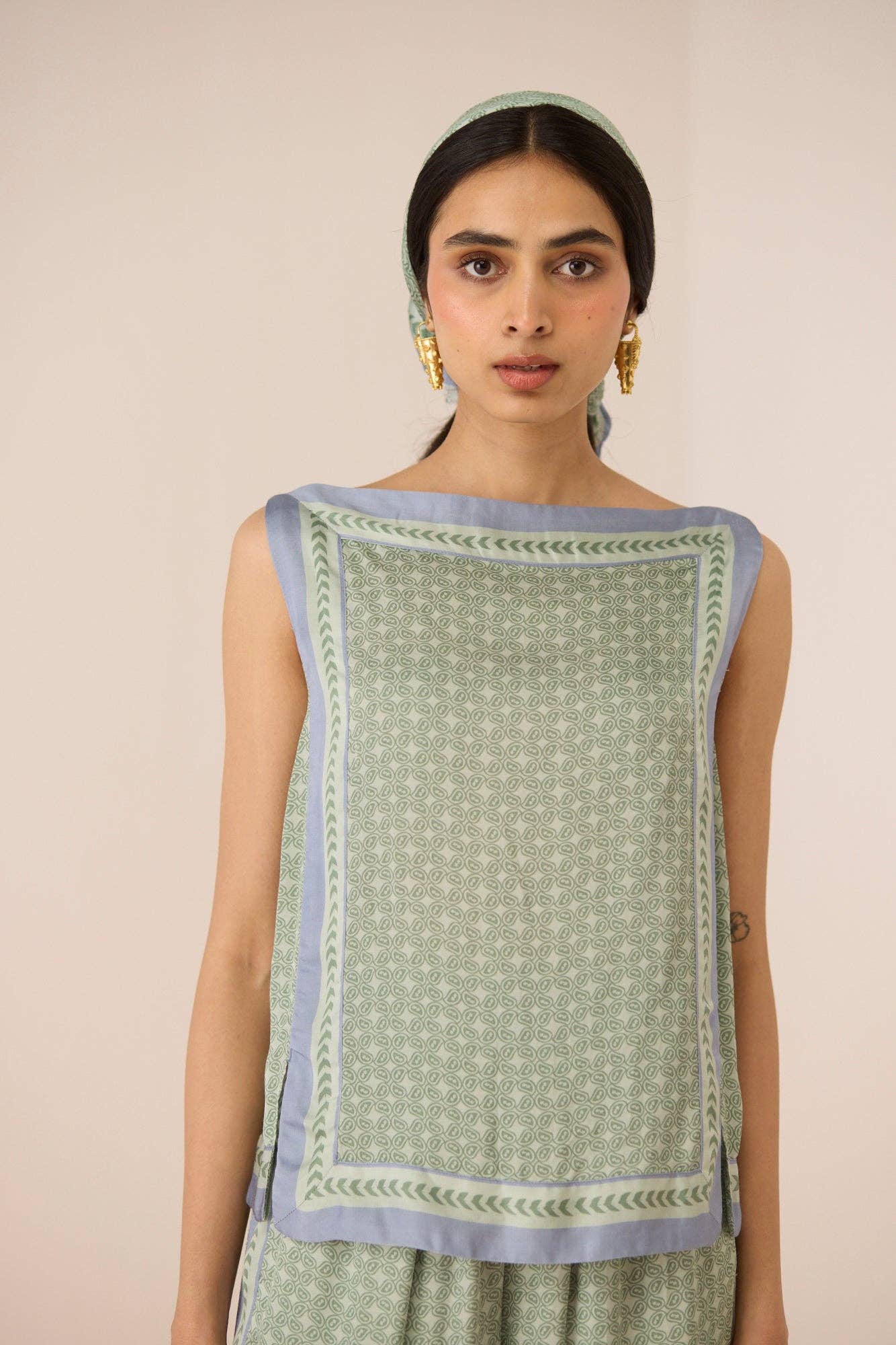 Woman wearing a green sleeveless top with a patterned border against a beige background