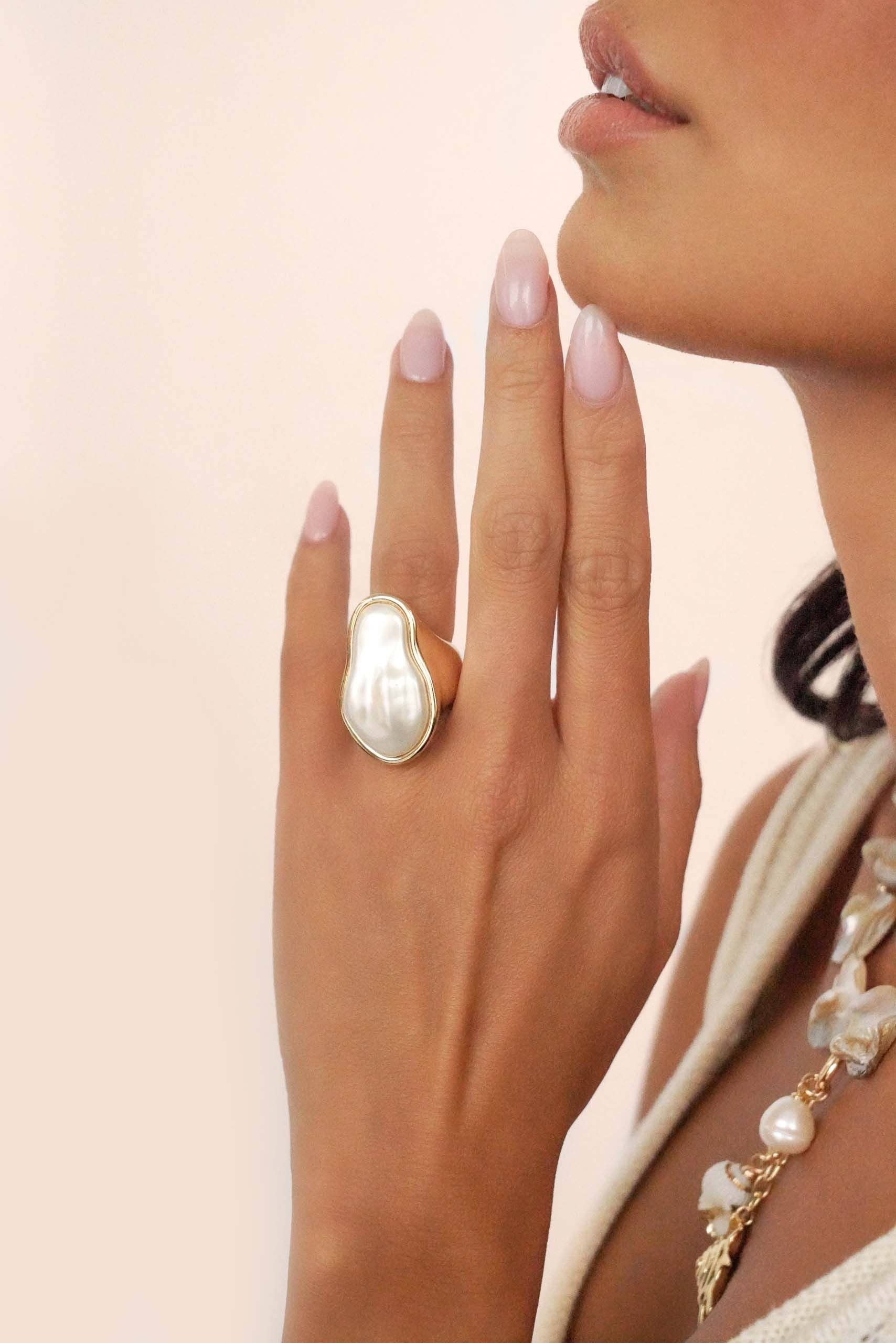 Woman's hand wearing a large pearl ring with a soft pink background