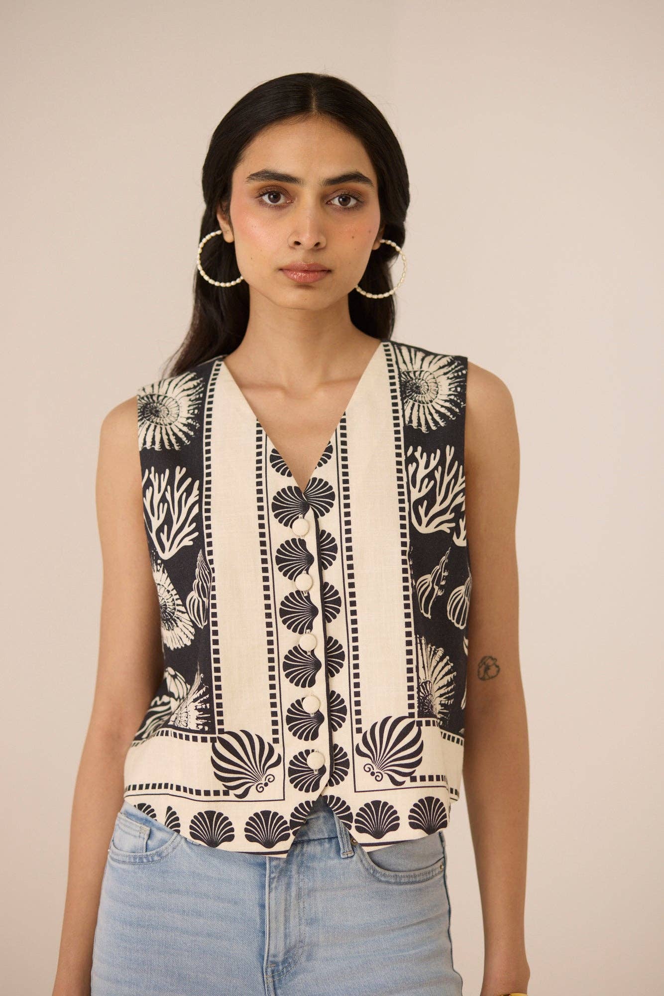 Woman wearing a sleeveless top with black and white pattern against a beige background