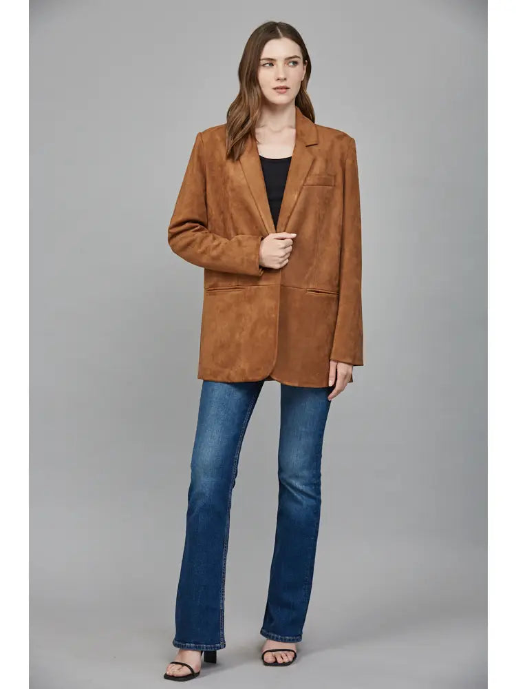 Woman wearing a brown blazer and blue jeans on a gray background
