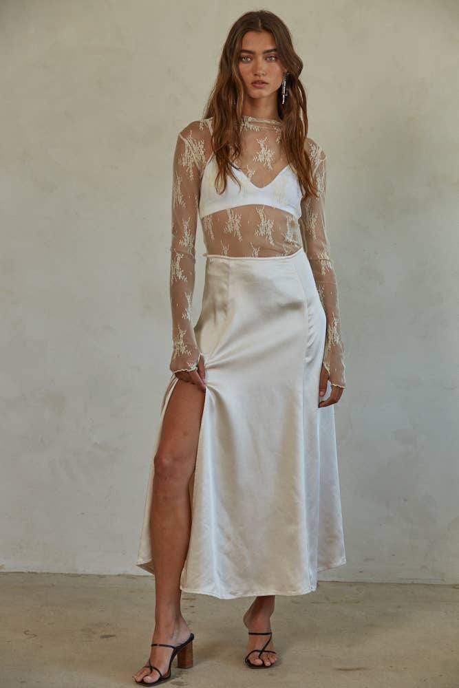 Woman wearing a white lace top and satin skirt against a plain background