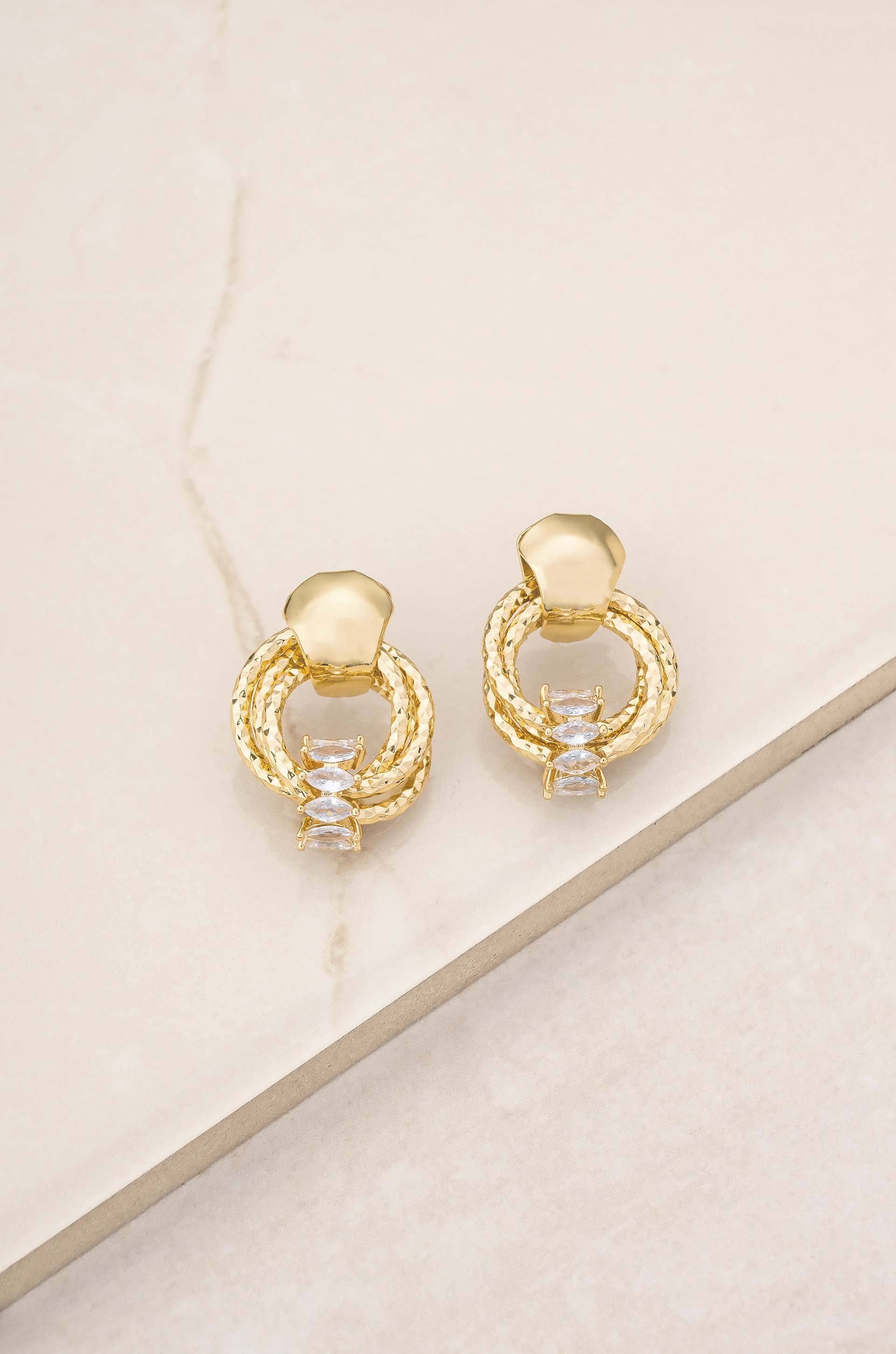 Gold hoop earrings with small diamonds on a beige surface