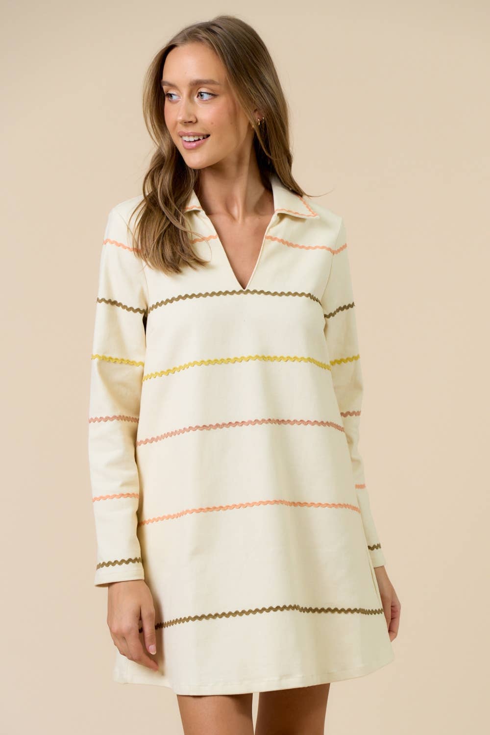 Add a touch of playful retro charm to your wardrobe with this cream collared mini dress. Designed with long sleeves and a relaxed A-line silhouette, it features soft zig-zag horizontal stripes in earthy tones of olive, peach, and mustard. The deep V-neckline with a pointed collar gives it a casual yet chic finish, making it an effortless piece for smart casual styling.
Cream base with multicolor wavy stripe detailing
Relaxed fit with long sleeves
Collared V-neckline for a modern retro vibe
Easy pullover