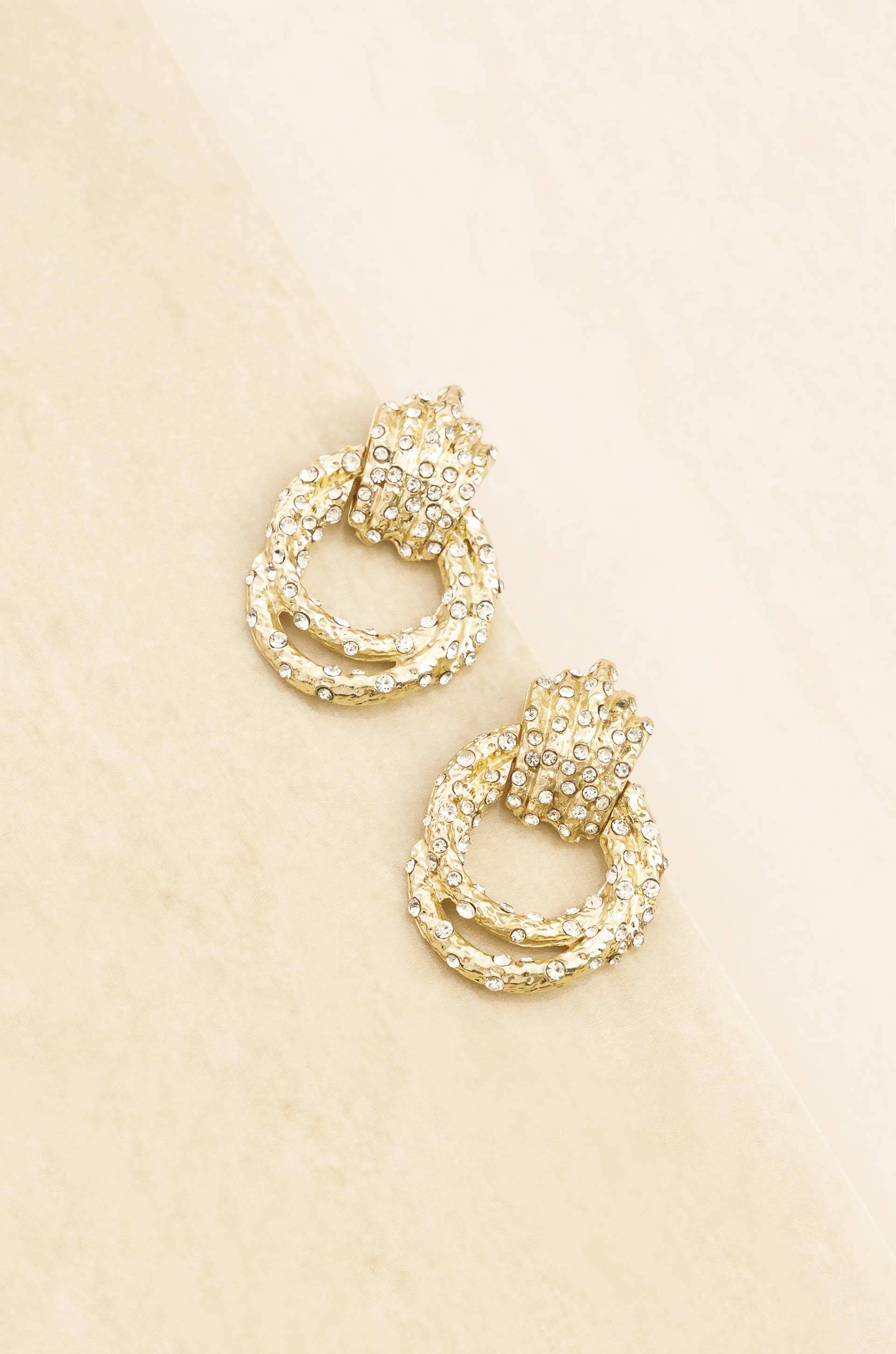 Gold hoop earrings with intricate detailing on a beige background