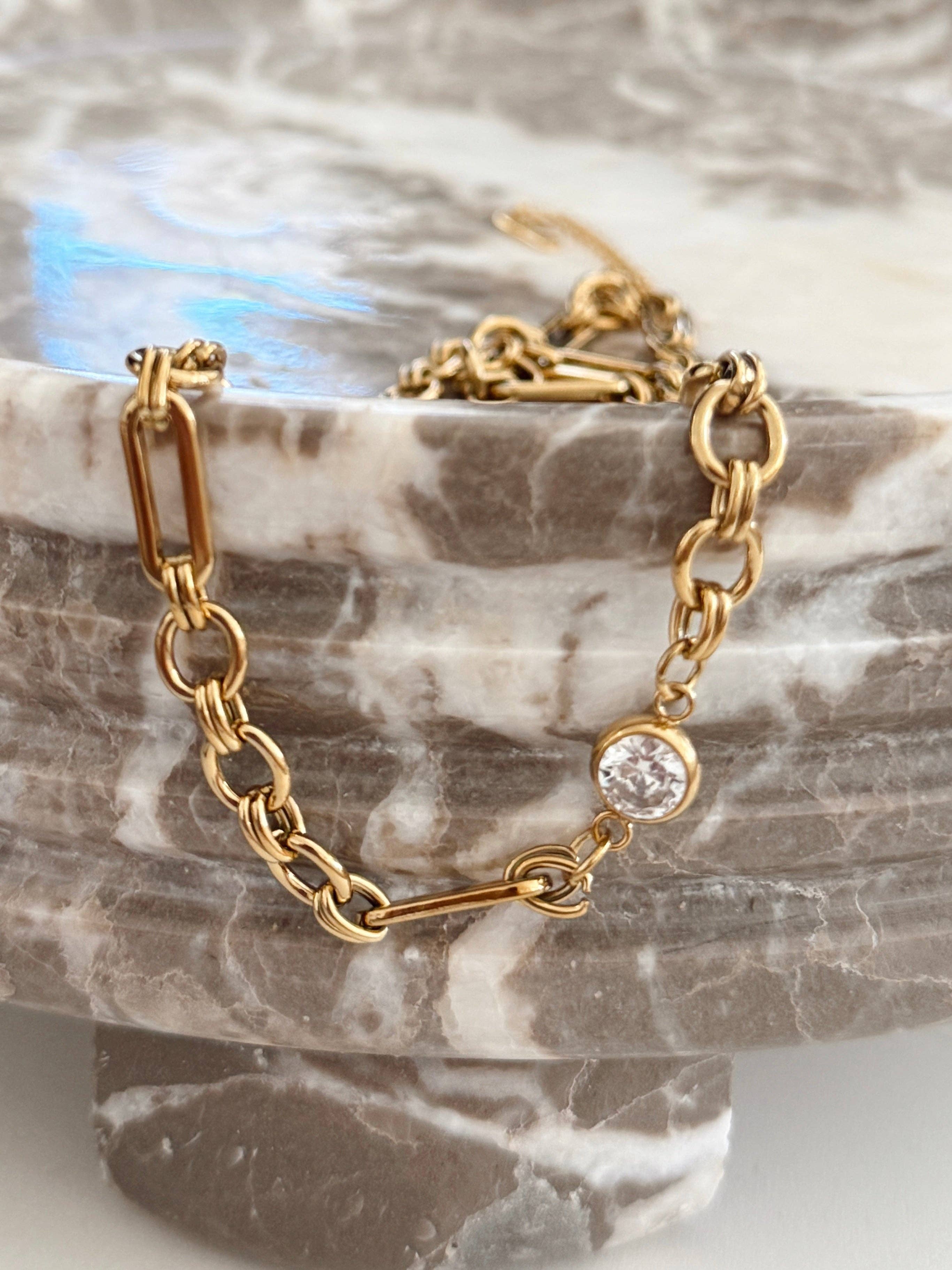 Gold chain bracelet with a clear gemstone on a marble surface