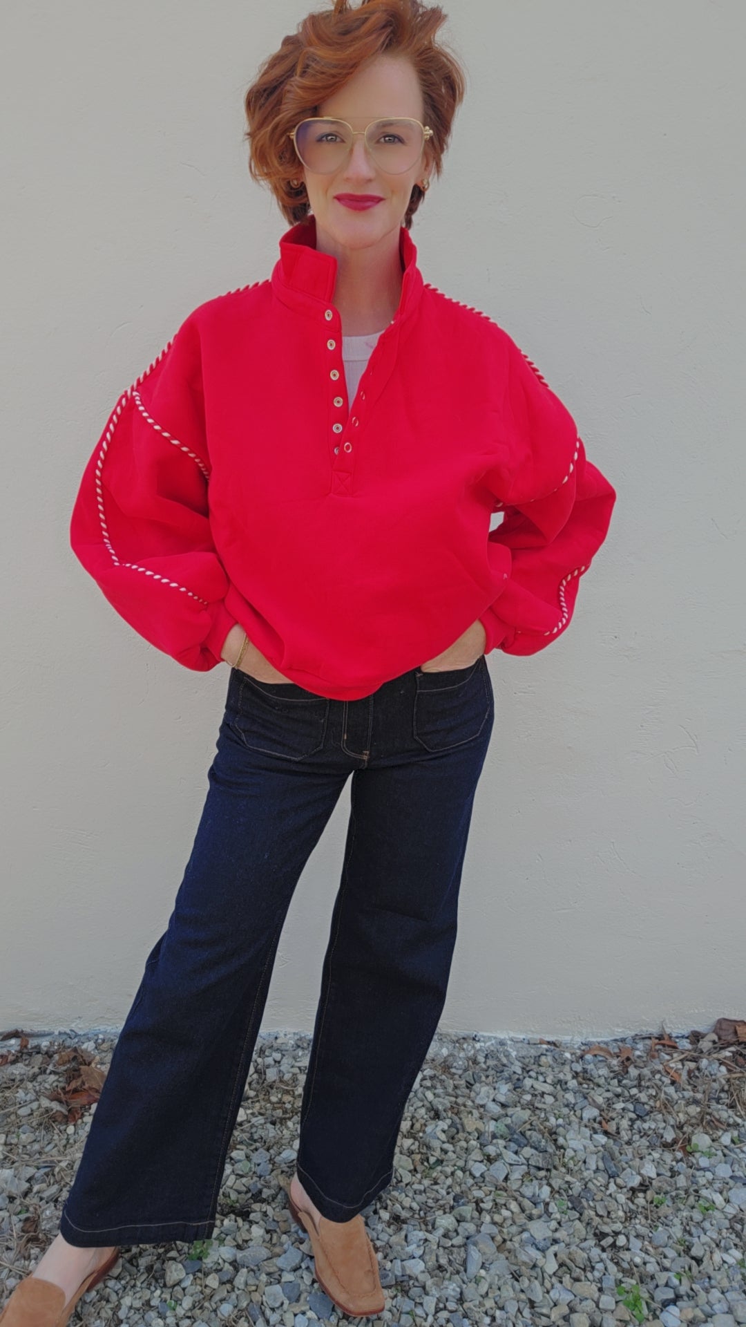 Person wearing a bright red sweater and dark jeans against a plain background