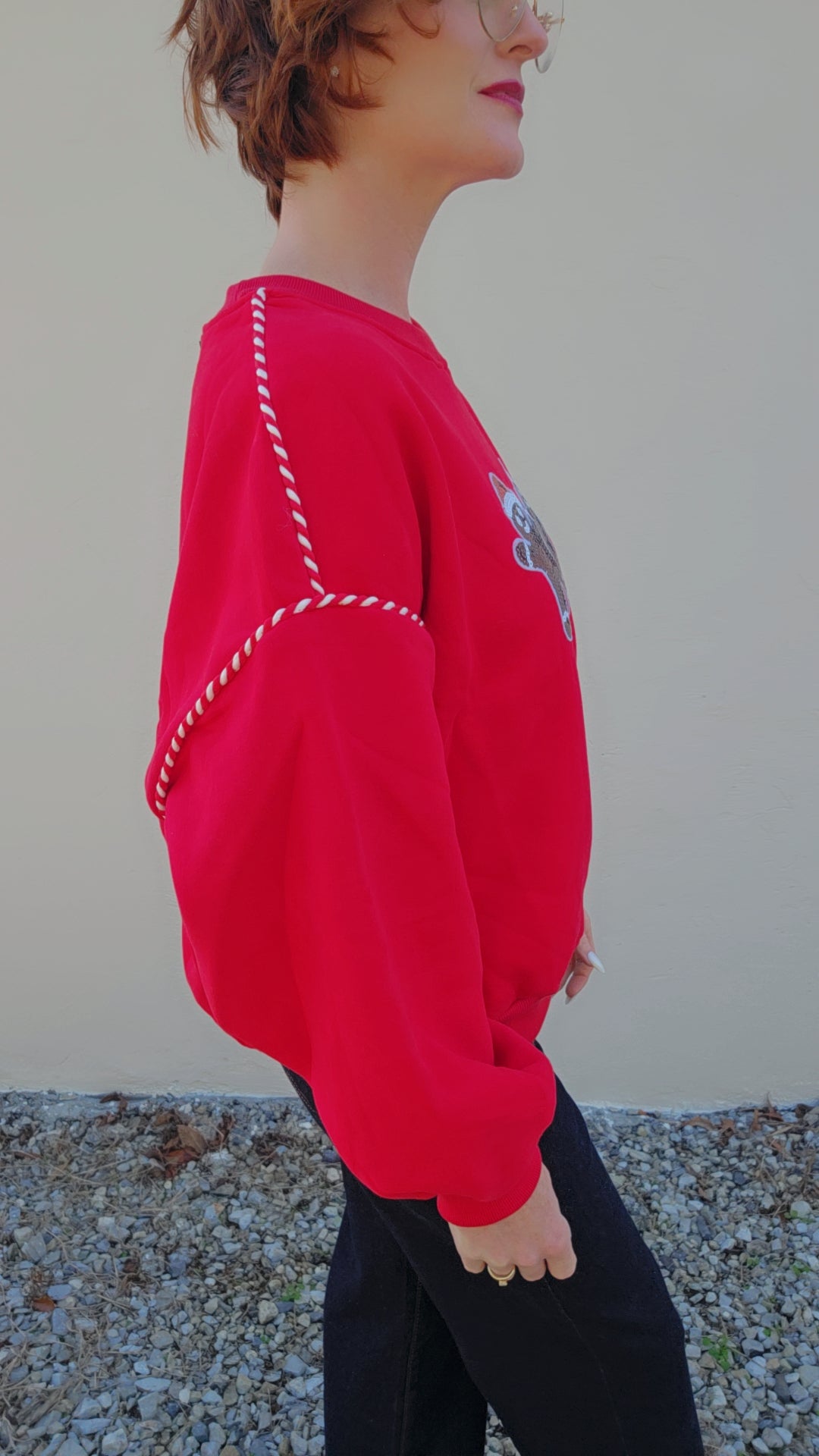 Person wearing a red sweater with white stitching detail against a plain background