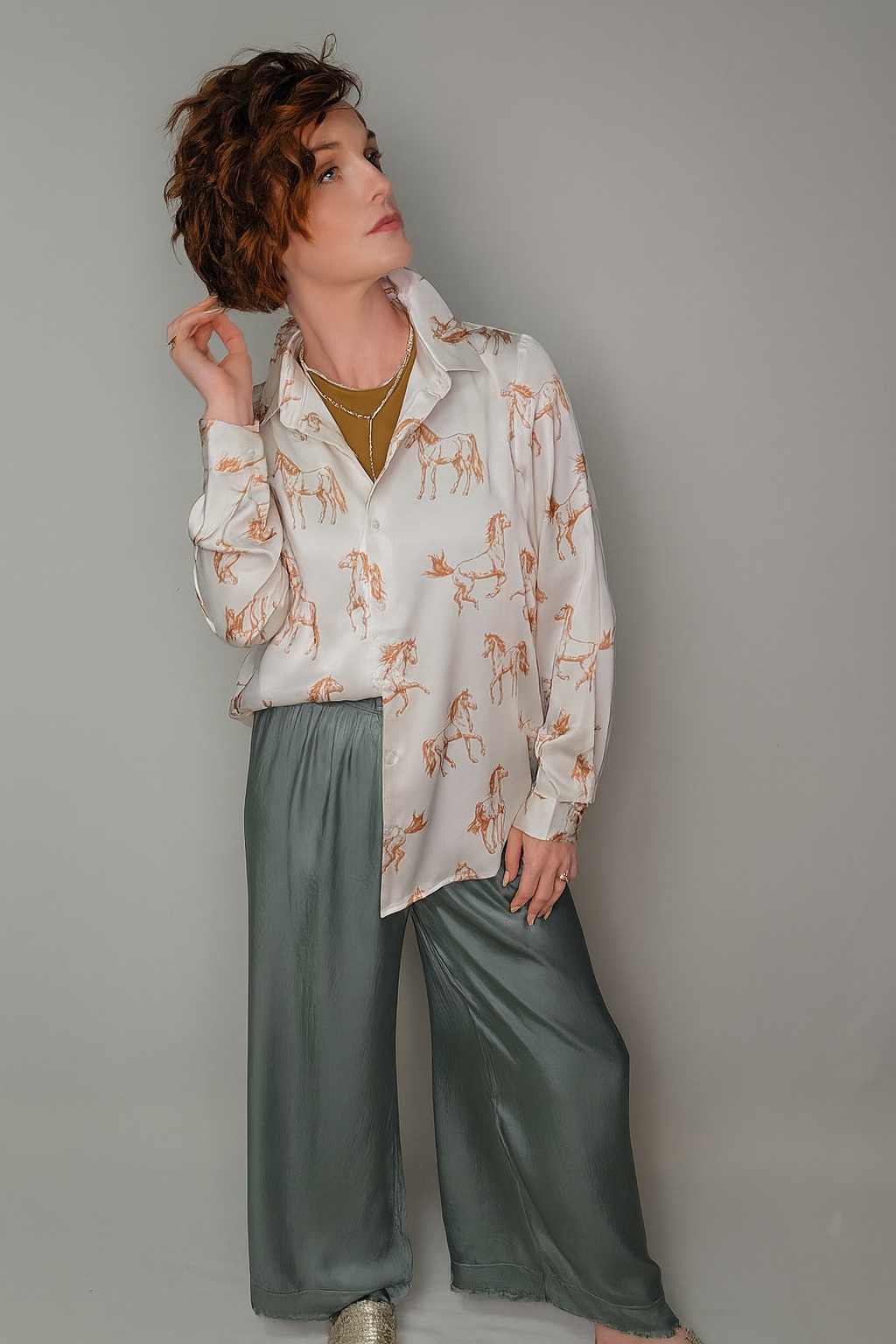 Woman wearing a patterned shirt and green pants against a gray background