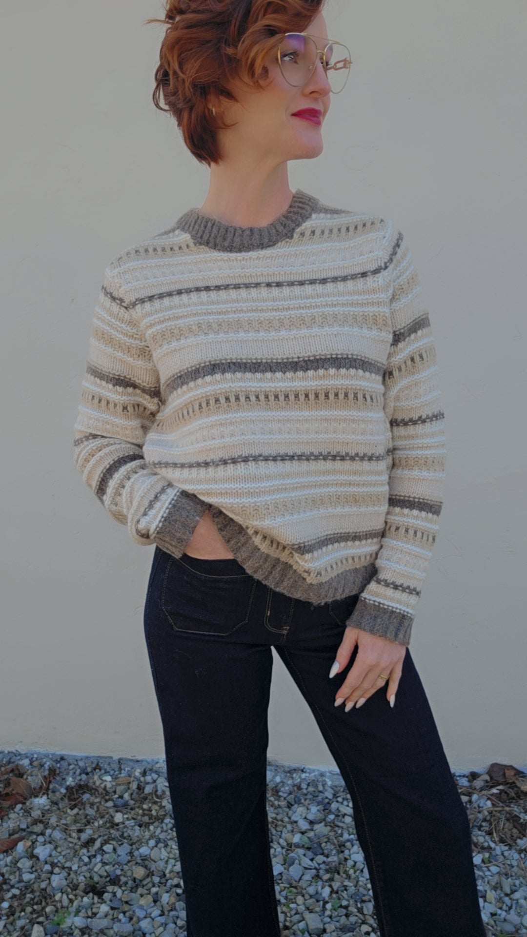 Person wearing a patterned sweater and dark jeans against a neutral background