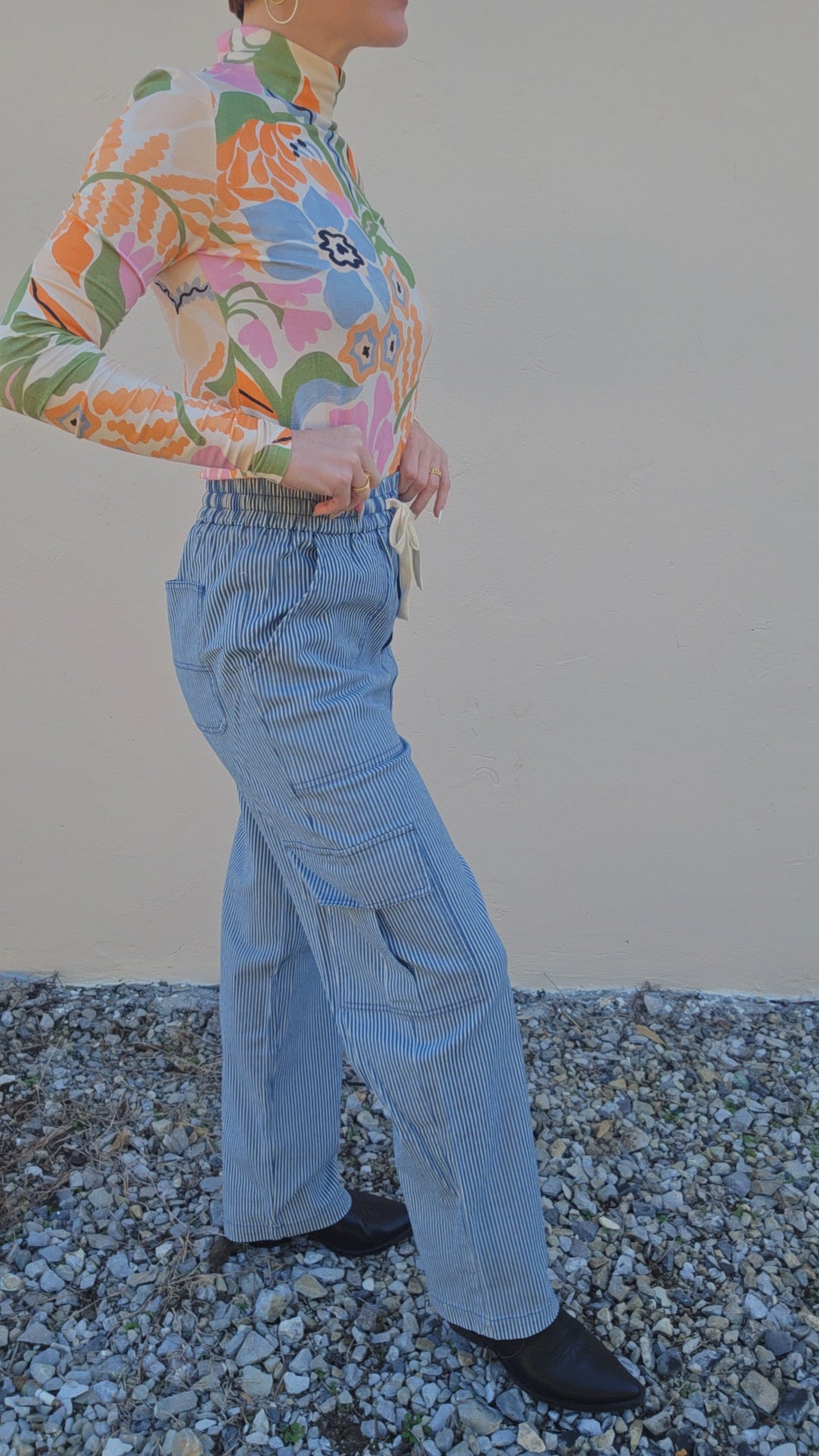 Person wearing a colorful floral shirt and light blue pants standing on a gravel surface.