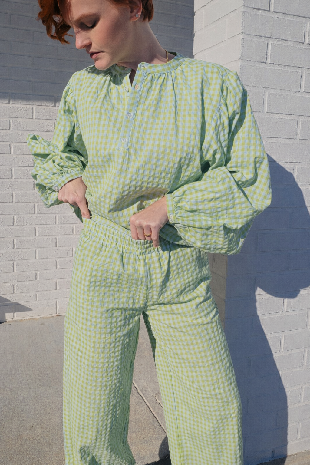 Person wearing a green patterned outfit standing against a brick wall.