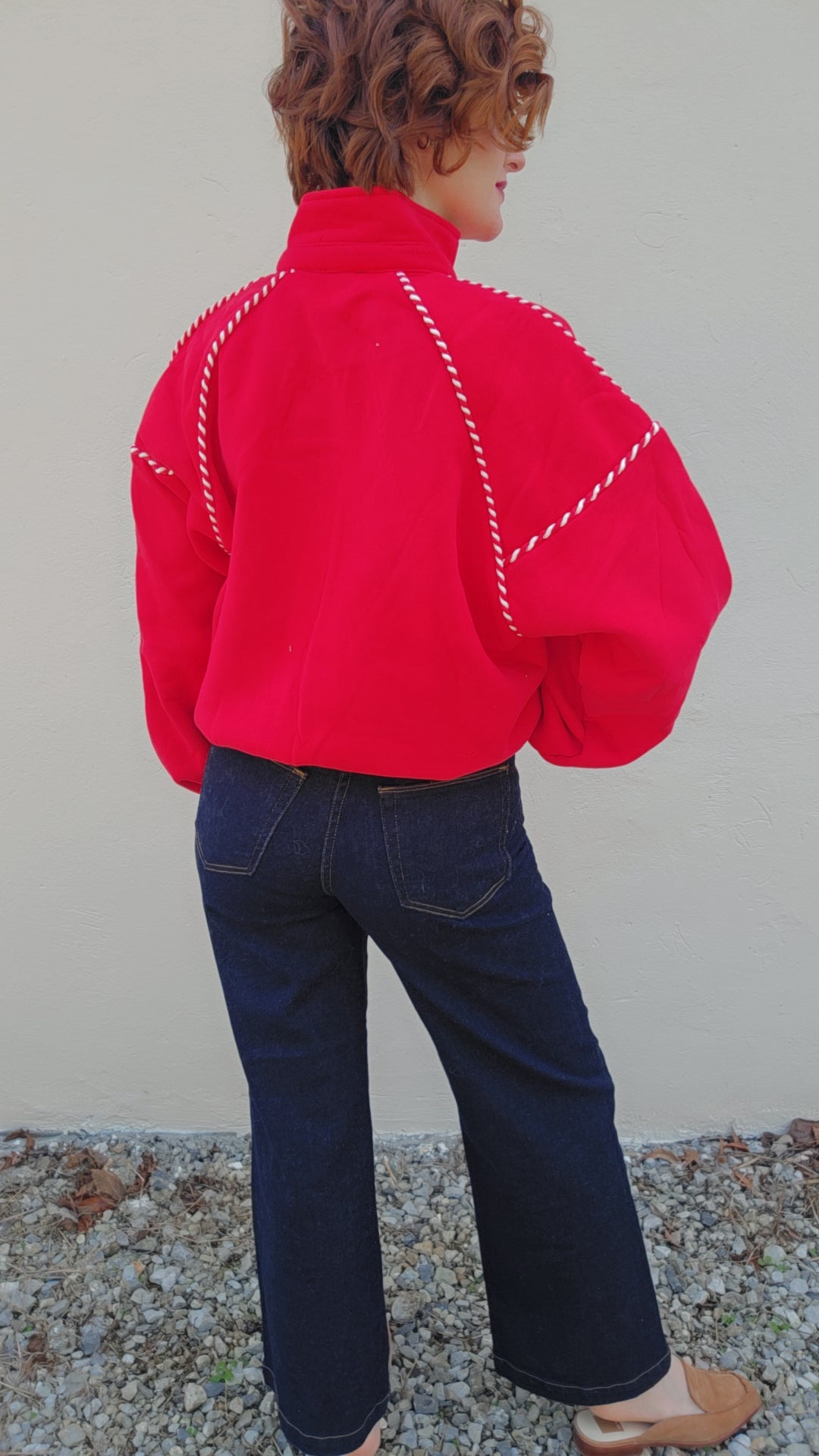 Person wearing a bright red jacket with white stitching and dark blue jeans against a plain background