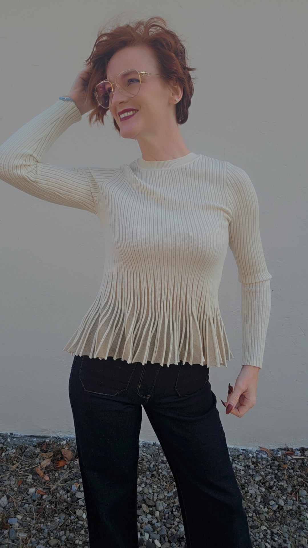 Woman wearing a beige ribbed sweater and black pants against a plain background