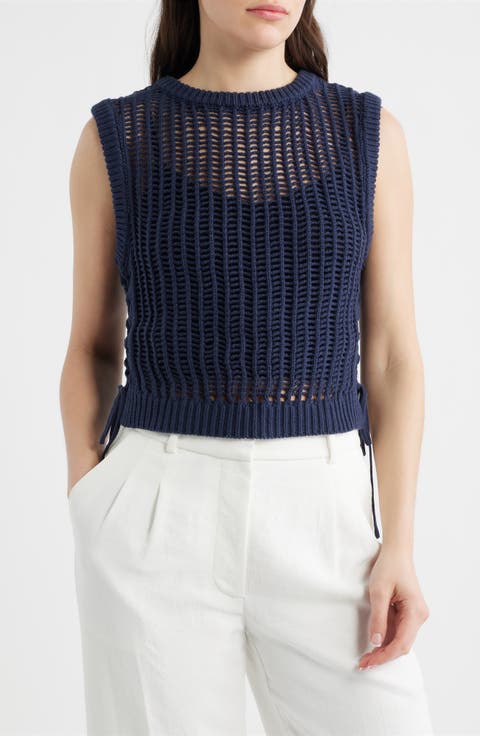 Woman wearing a navy blue sleeveless knitted top and white pants on a white background