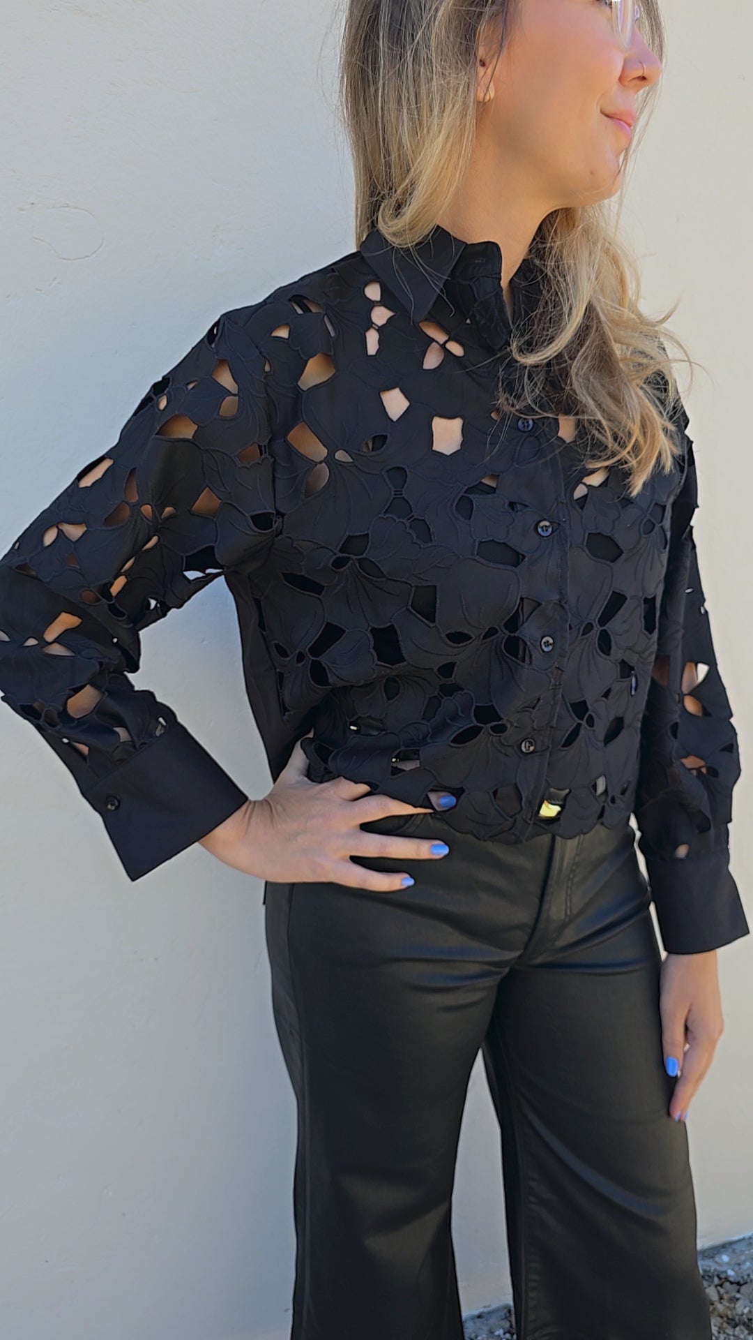 Woman wearing a black perforated blouse against a white wall
