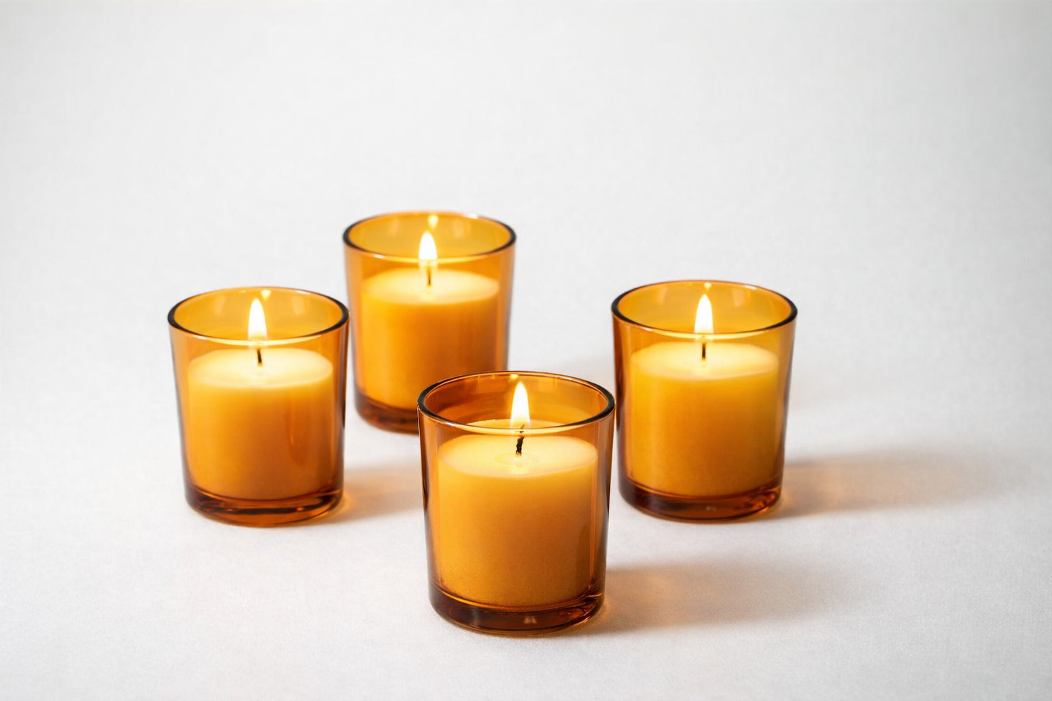 Four lit candles in amber glass holders on a white background